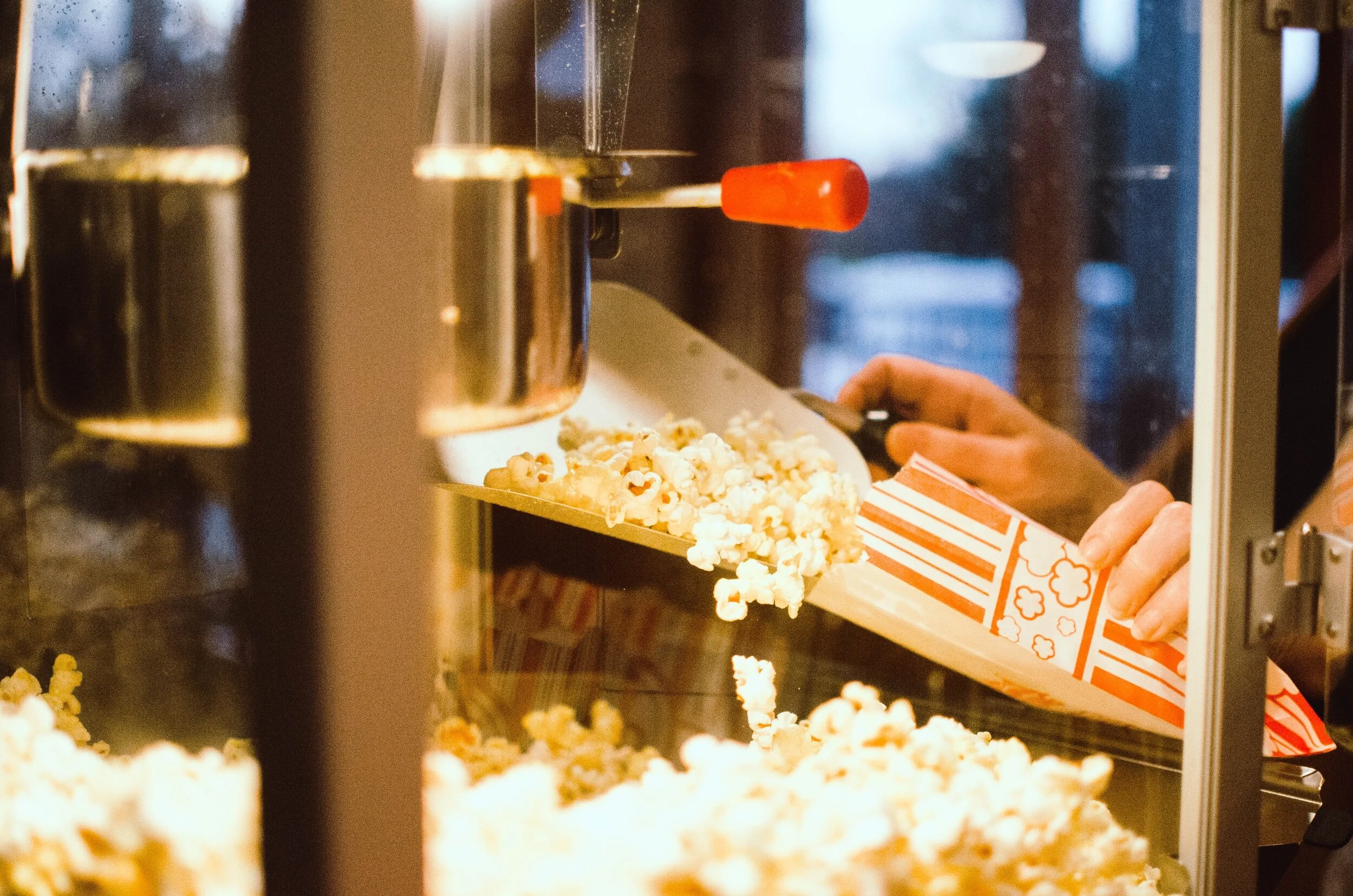 Employee at a movie theater scoops popcorn into a bag