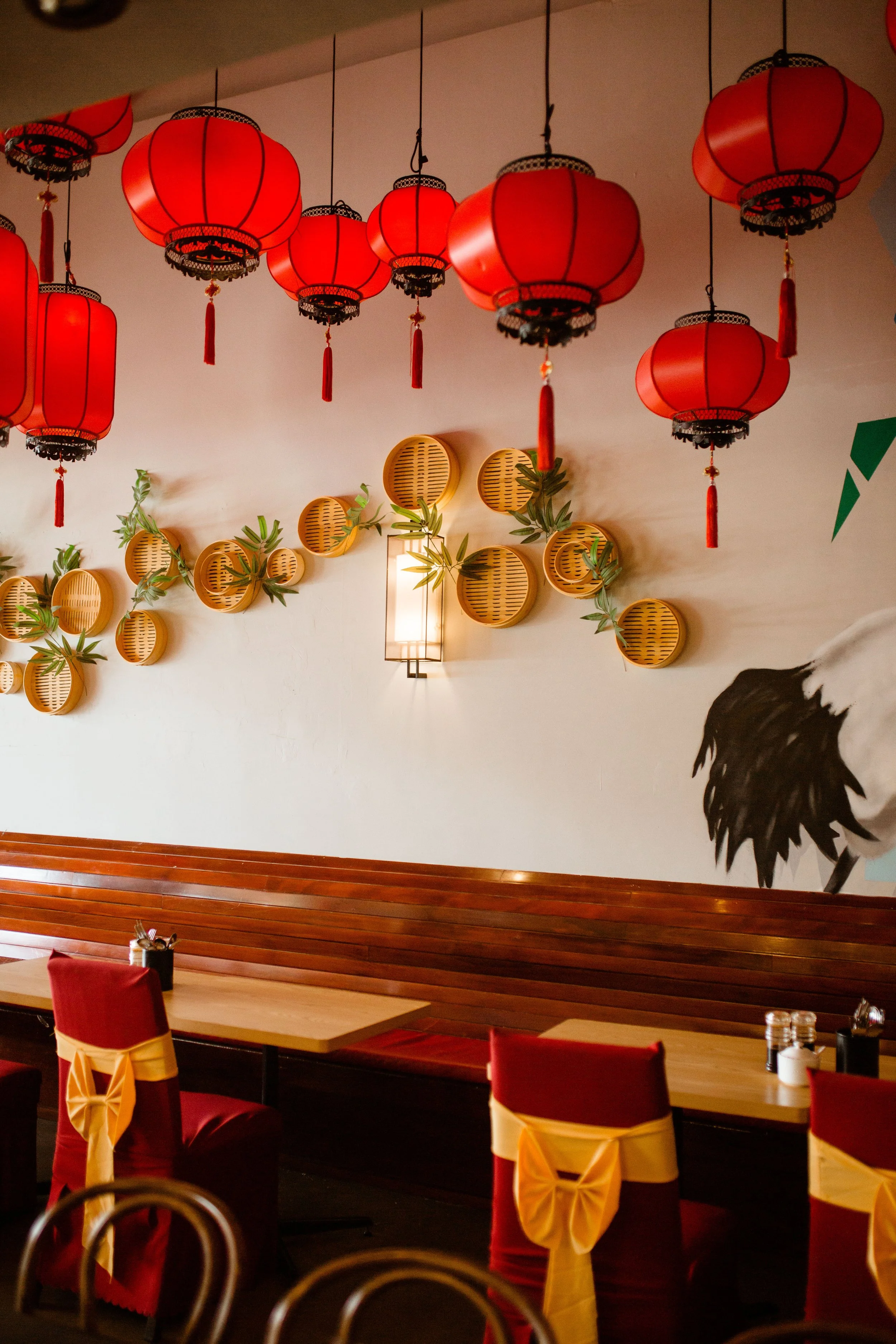 Decorative red Chinese lanterns hanging from ceiling inside restaurant with wall art featuring bamboo baskets and a black and white bird illustration.