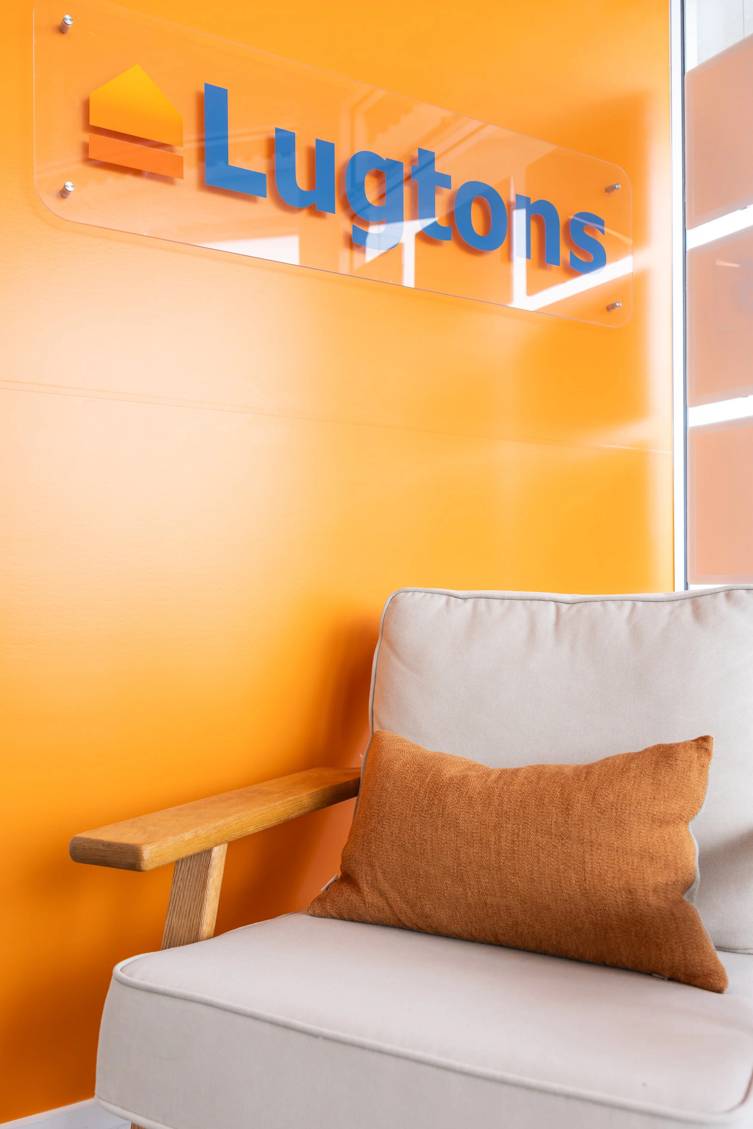 Interior of an office lobby with an orange wall, a sign that says "Lugtons," and a beige sofa with an orange pillow.