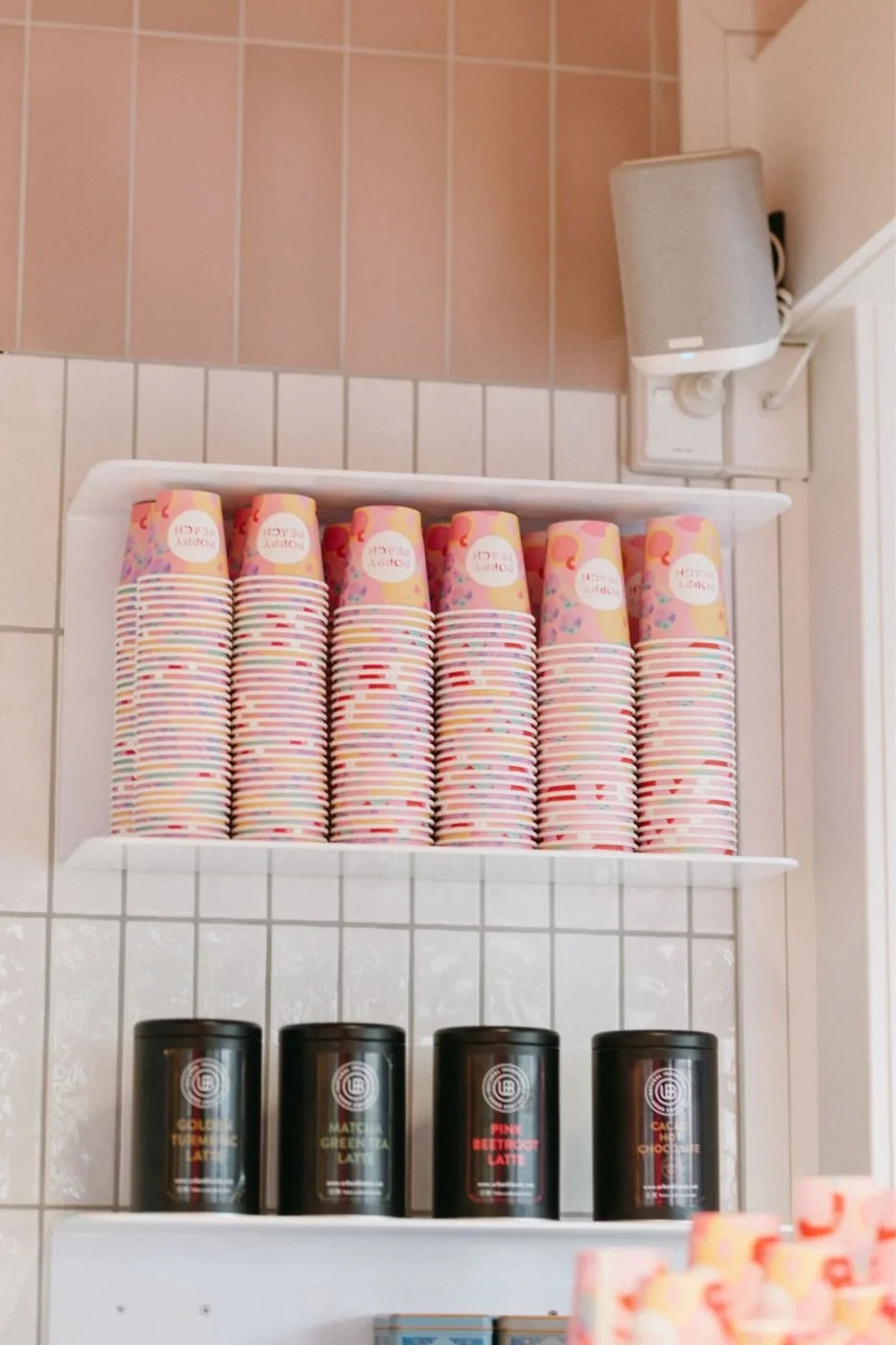 A display shelf with colorful paper cups on top and black tins below, set against tiled walls.
