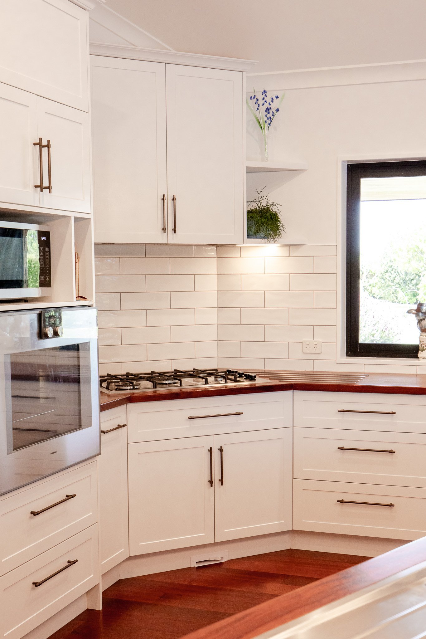 Kitchen with white cabinets, a window, and a small corner shelf with a plant and flowers.