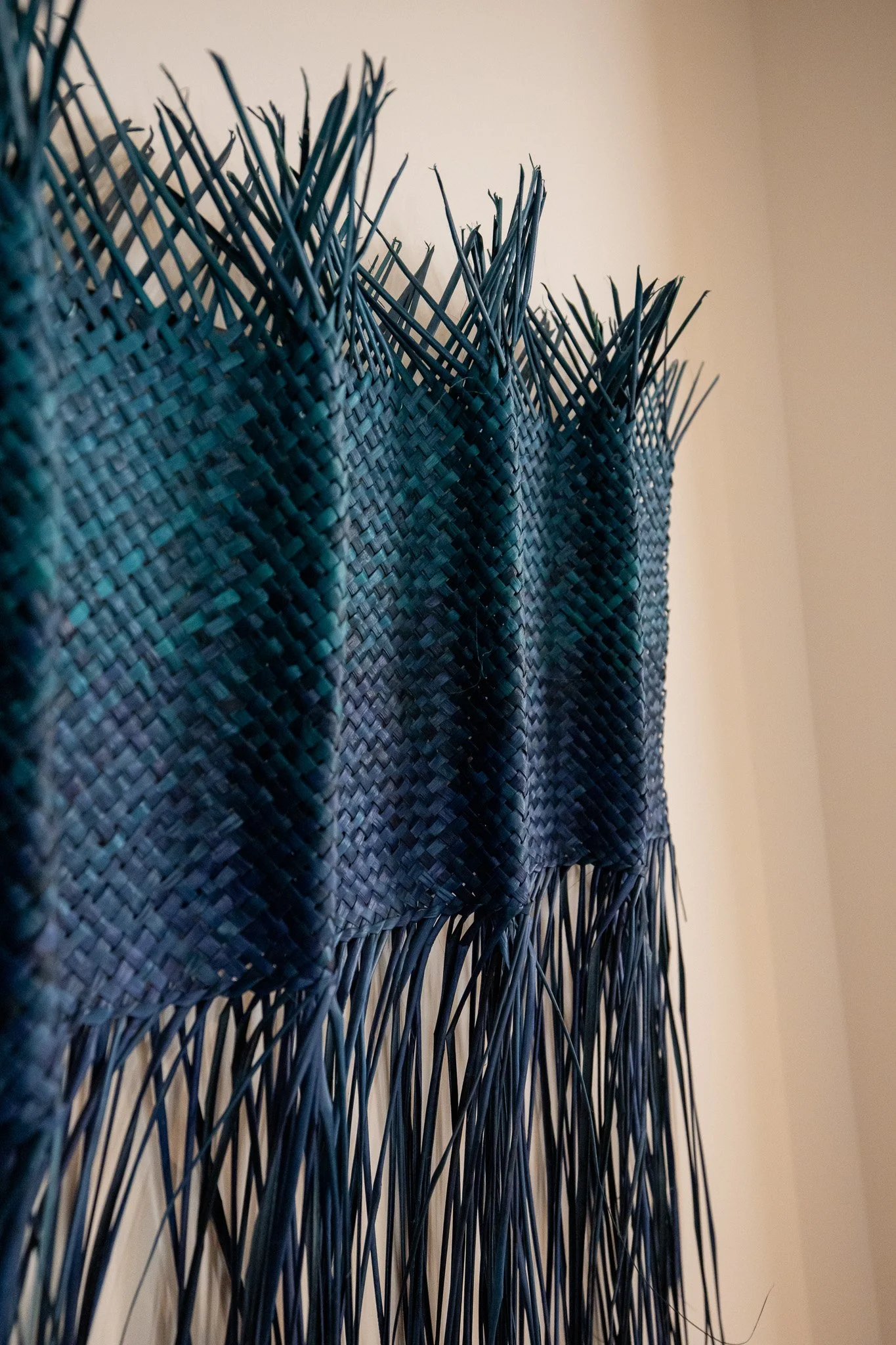 Close-up of a woven black basket with long, slender, and pointed straw-like decorations protruding from the top and bottom.