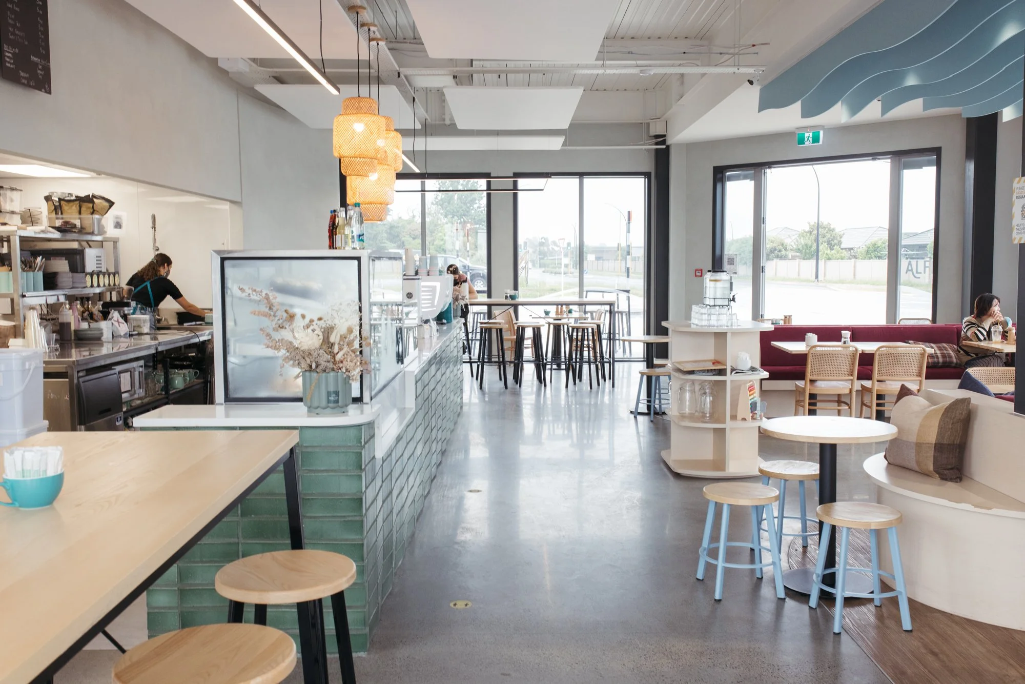 Modern cafe interior with a clean and bright atmosphere, featuring a counter with a barista, tables and chairs, large windows letting in natural light, and minimalistic decor.