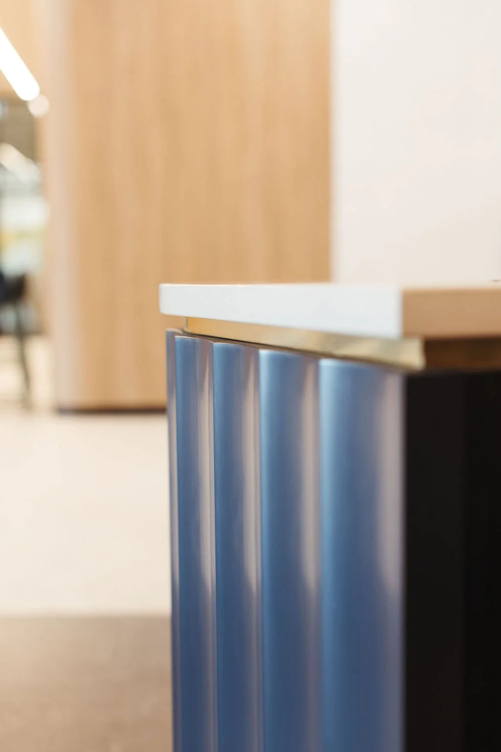 Close-up of a modern table edge with a white top and metallic blue support legs in an indoor space.
