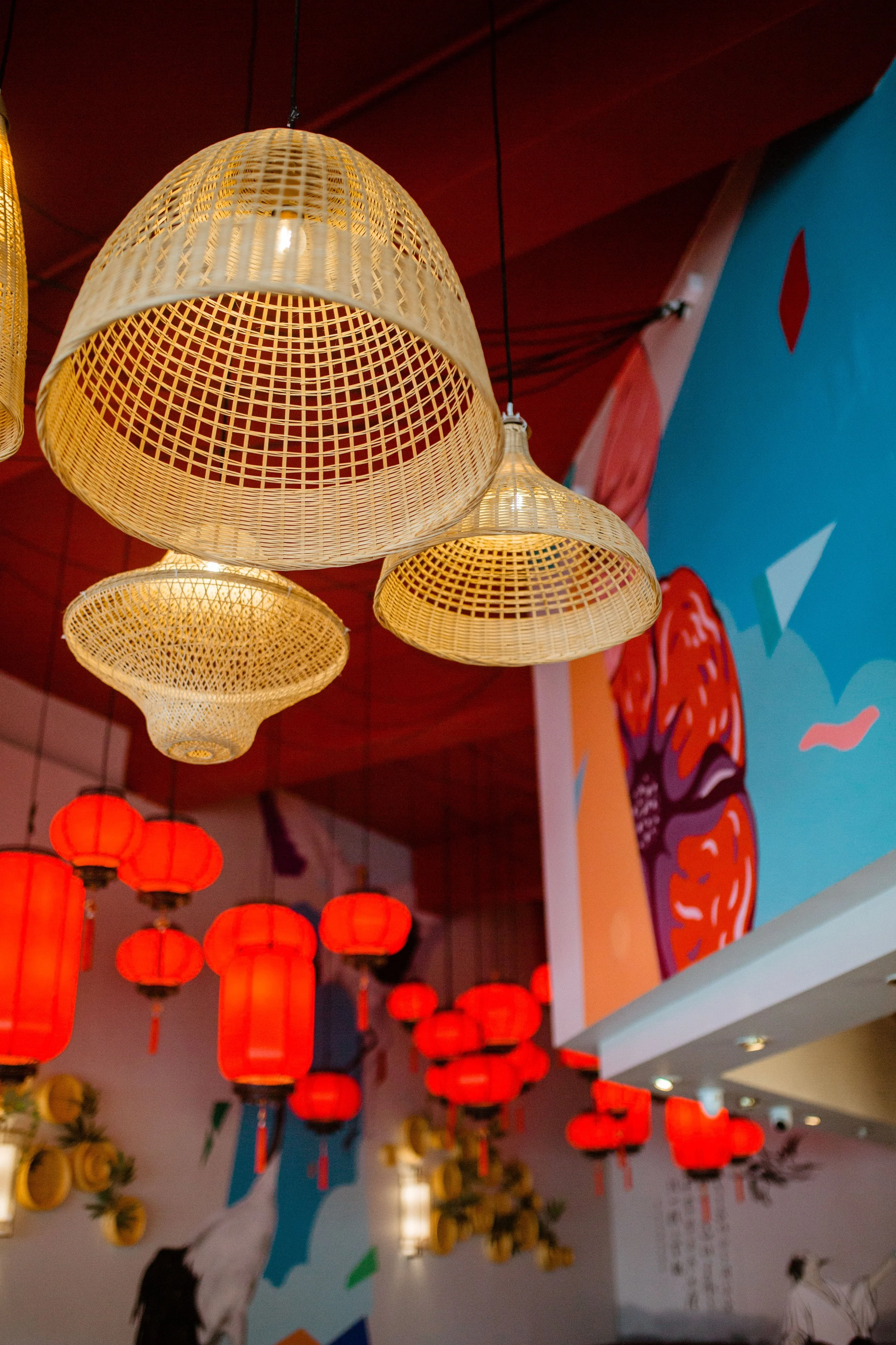 Decorative hanging lamps, including rattan and red lantern styles, in a vibrant indoor setting with colorful mural art on the wall.