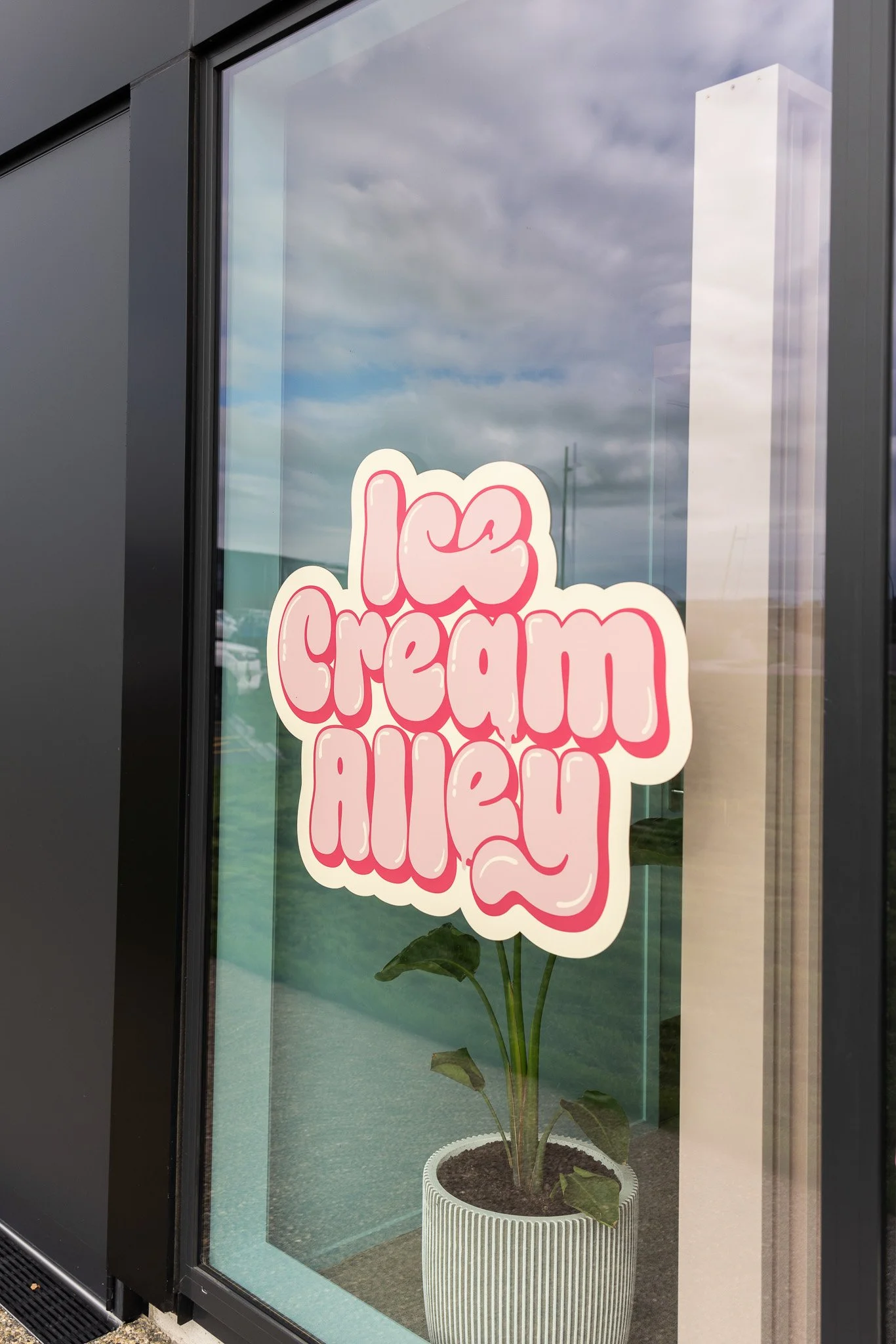 Sign in a window that says 'Ice Cream Alley' with a plant in a white pot beneath it.