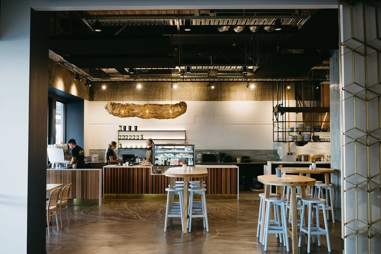 Interior of a modern coffee shop with a wooden counter, seating, and staff preparing drinks.