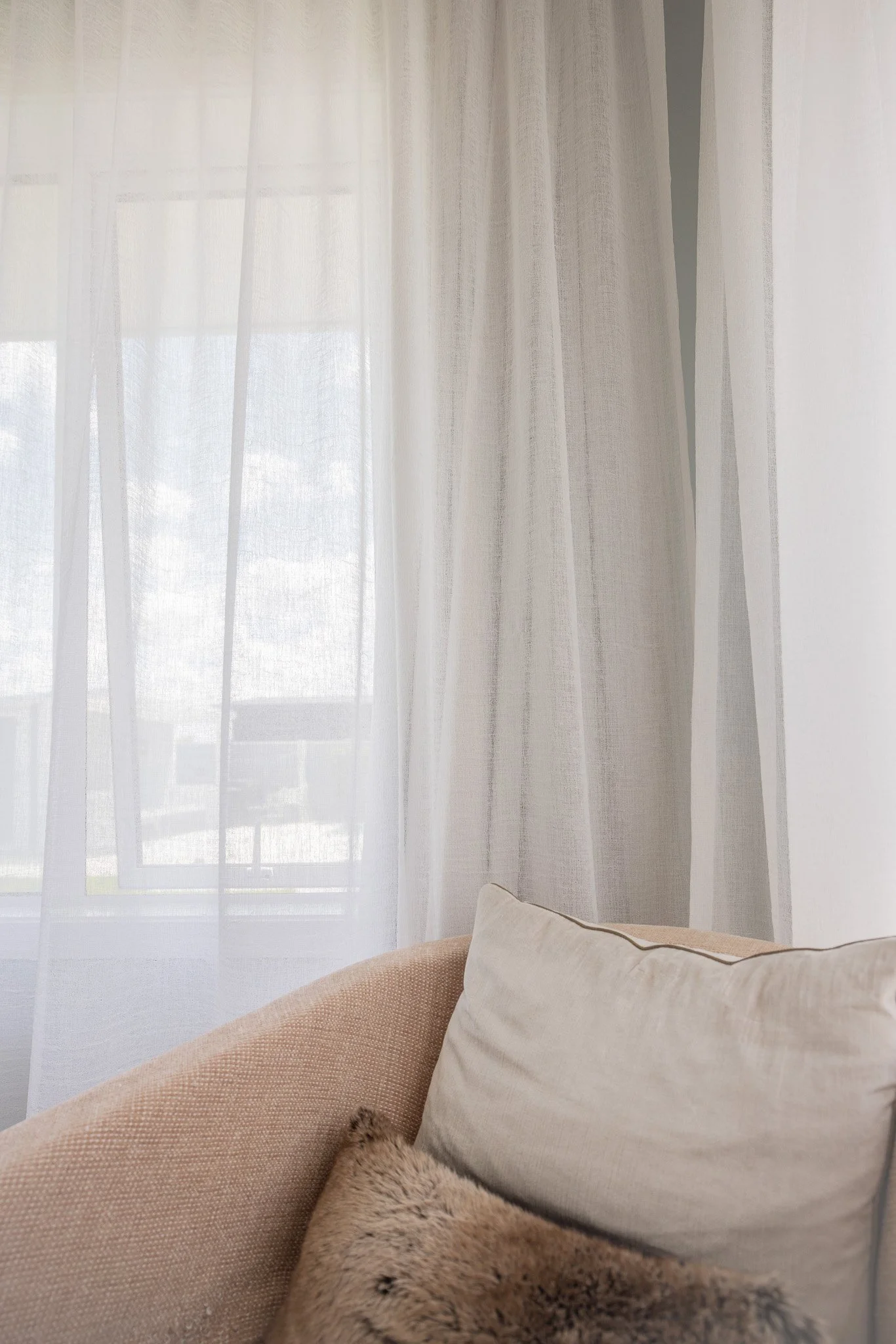 Living room corner with beige sofa, white pillows, and curtains covering a window.