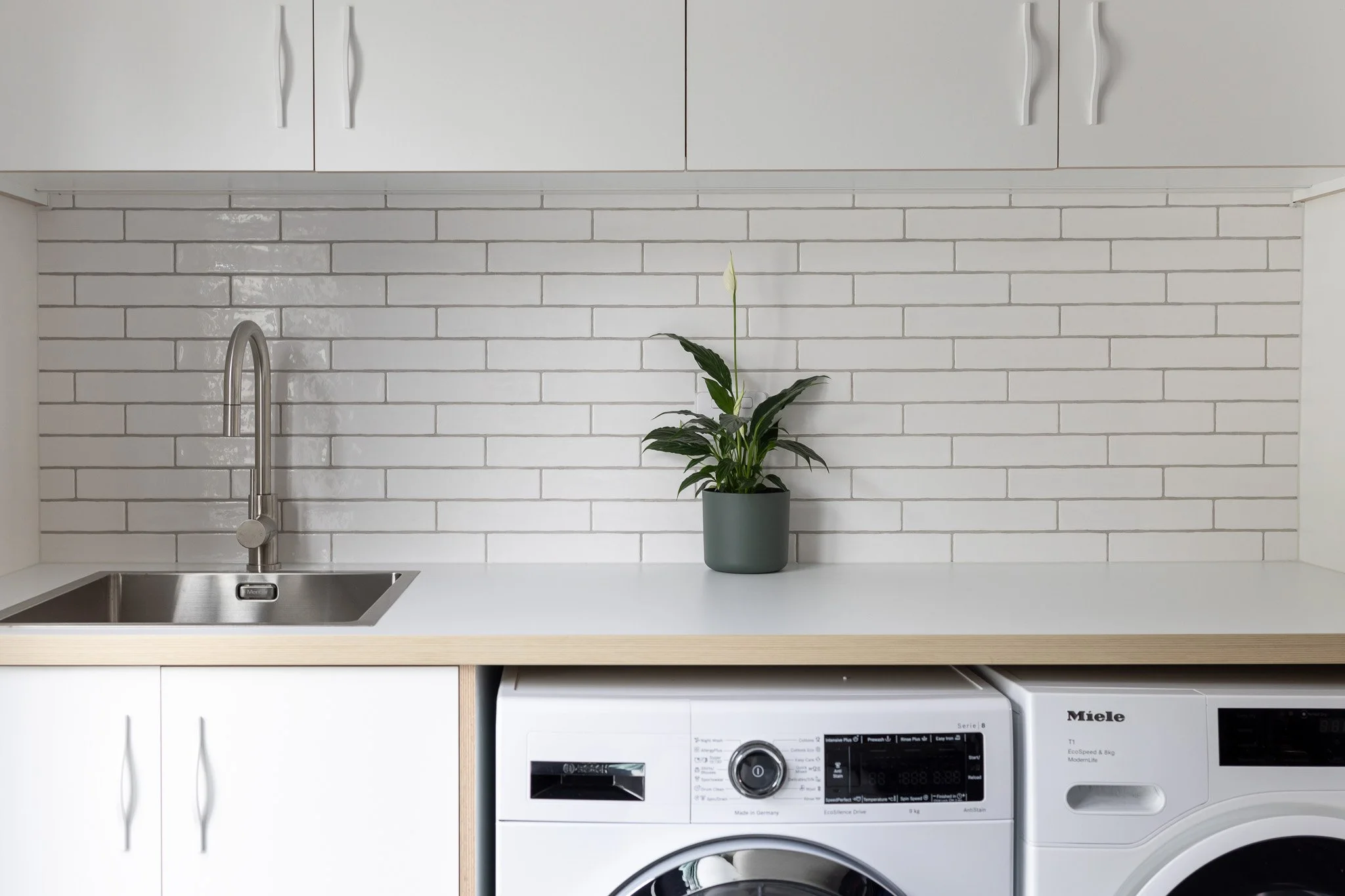 Laundry room with white cabinets, a stainless steel sink, a faucet, a potted plant on the countertop, and a white washing machine.