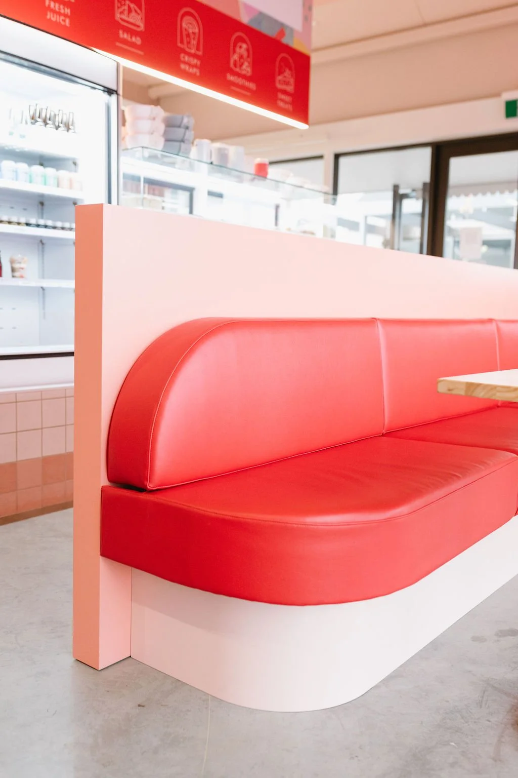 Red booth seating inside a breakfast restaurant or diner with a pink partition and a yellow wooden table.