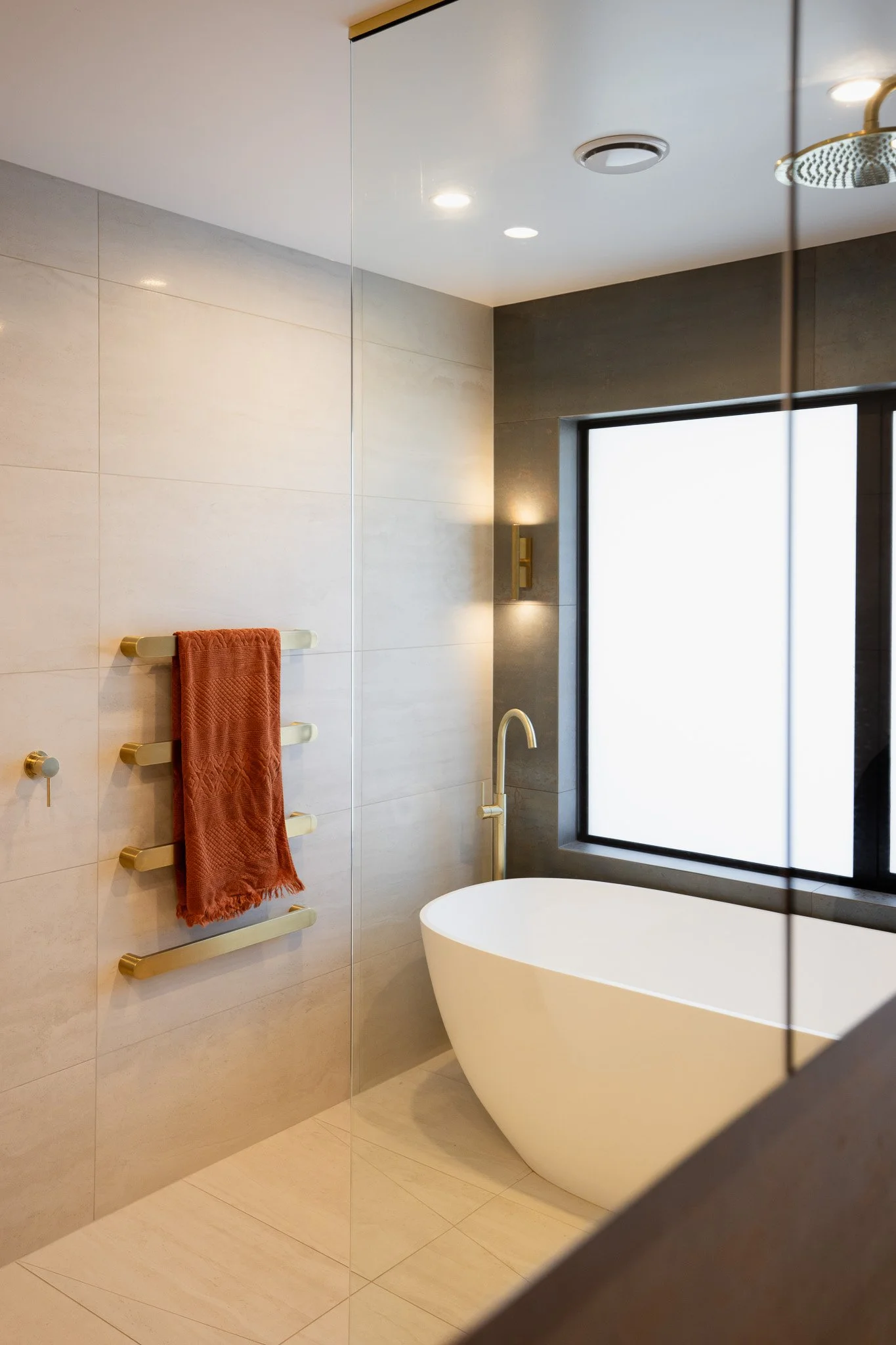 Modern bathroom with a freestanding bathtub, a large window, a wall-mounted towel rack with an orange towel, and minimal decor.