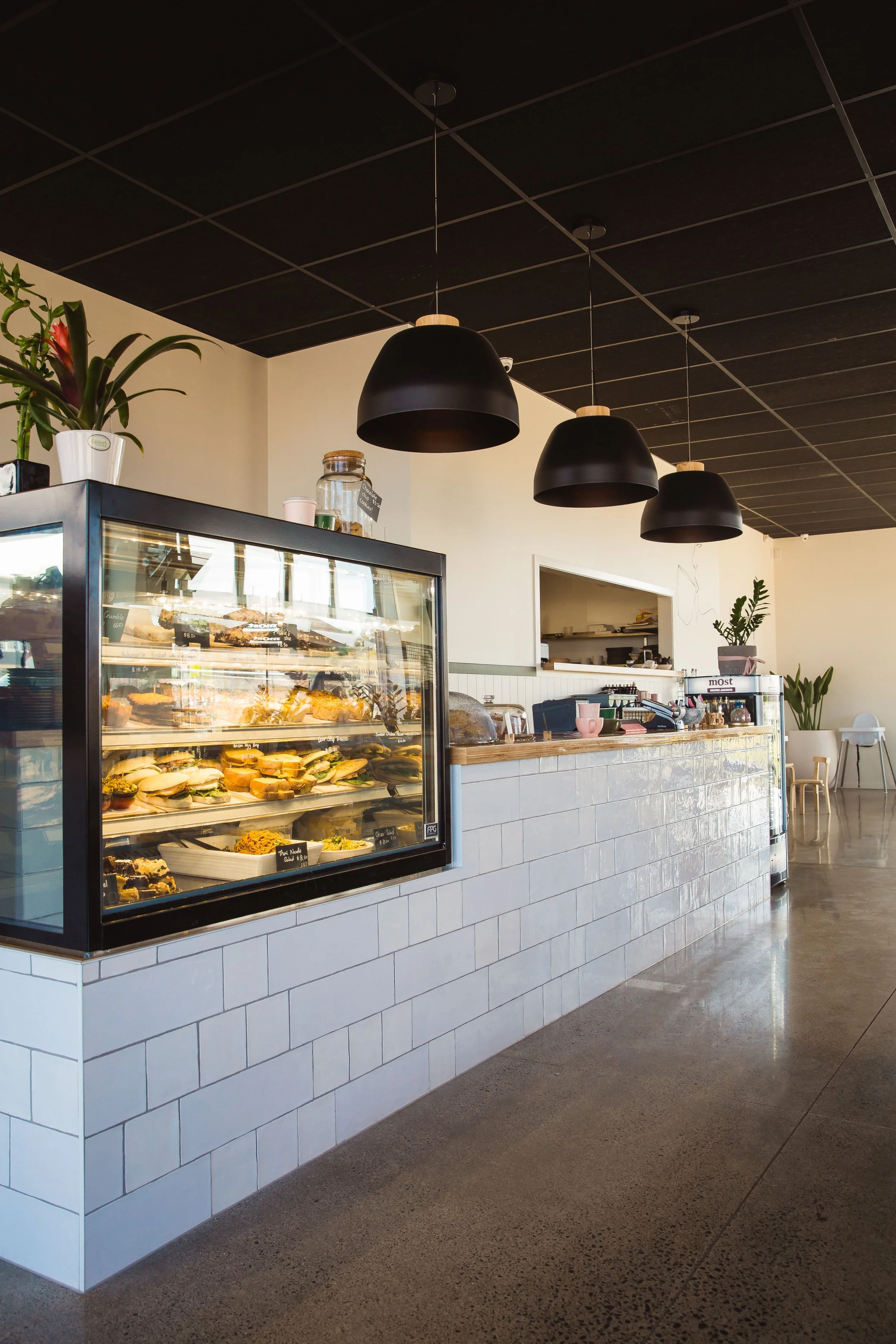 Modern cafe interior with a display case of baked goods, black hanging pendant lights, and minimalist decor.