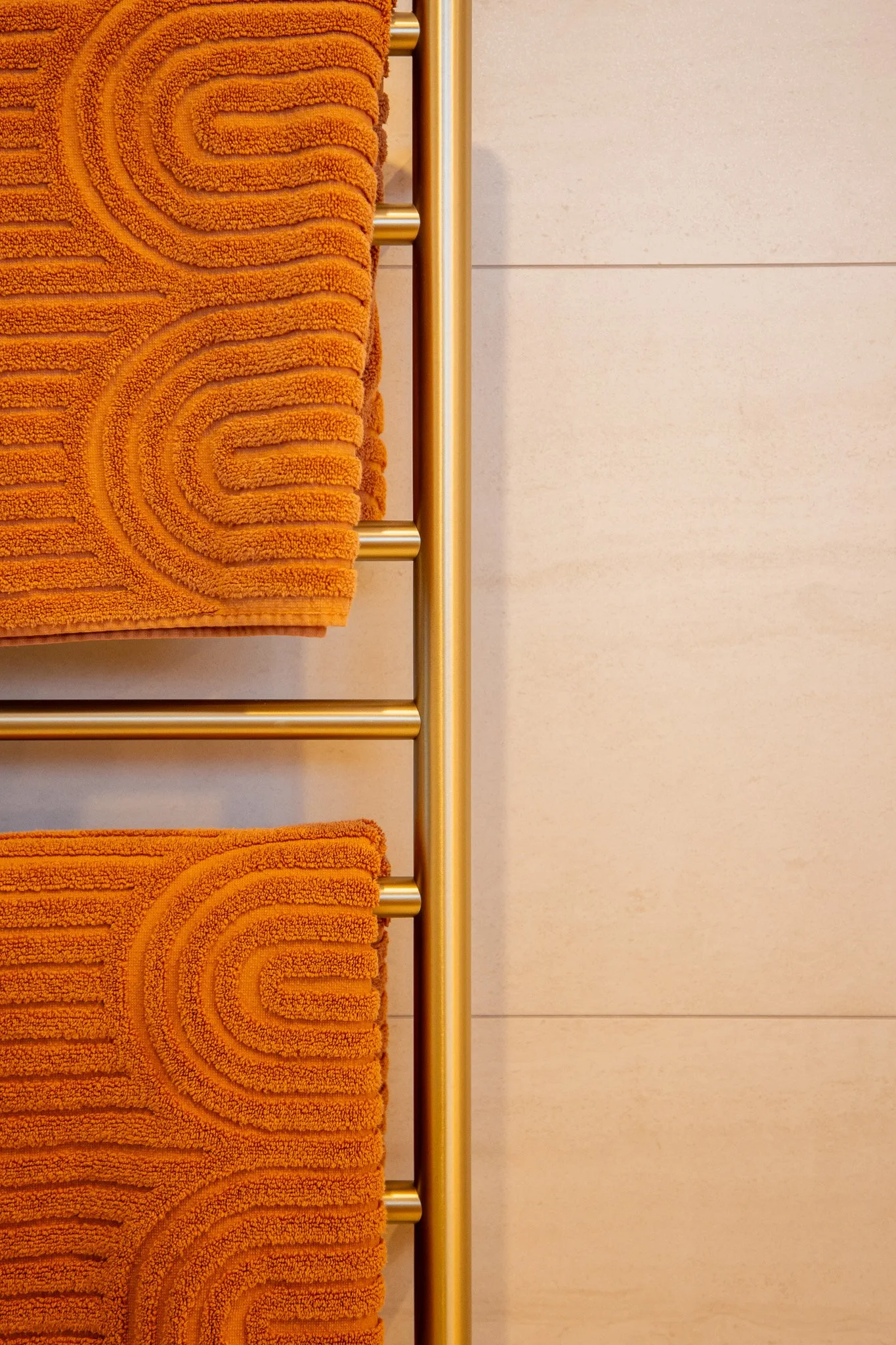 Two orange towels with textured patterns hanging on a gold towel rack against a light-colored wall.