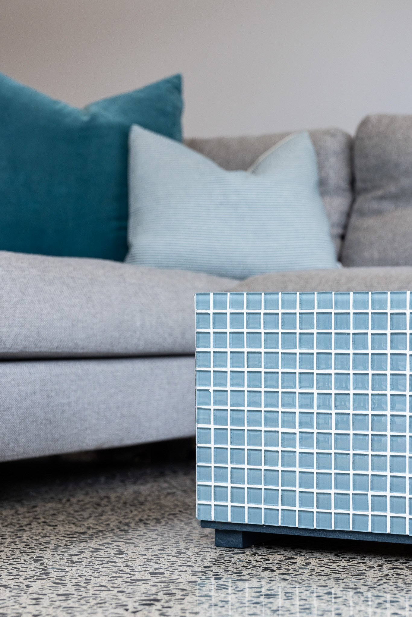 A tiled blue and white cabinet with a grey sofa and blue cushions in the background.