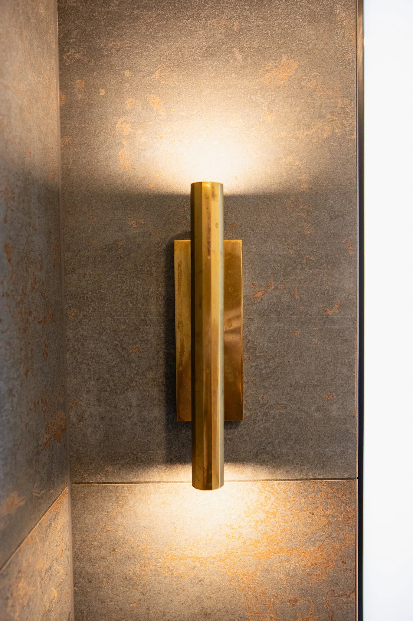 Close-up of a modern, gold-colored door handle mounted on a textured, rustic metal door.