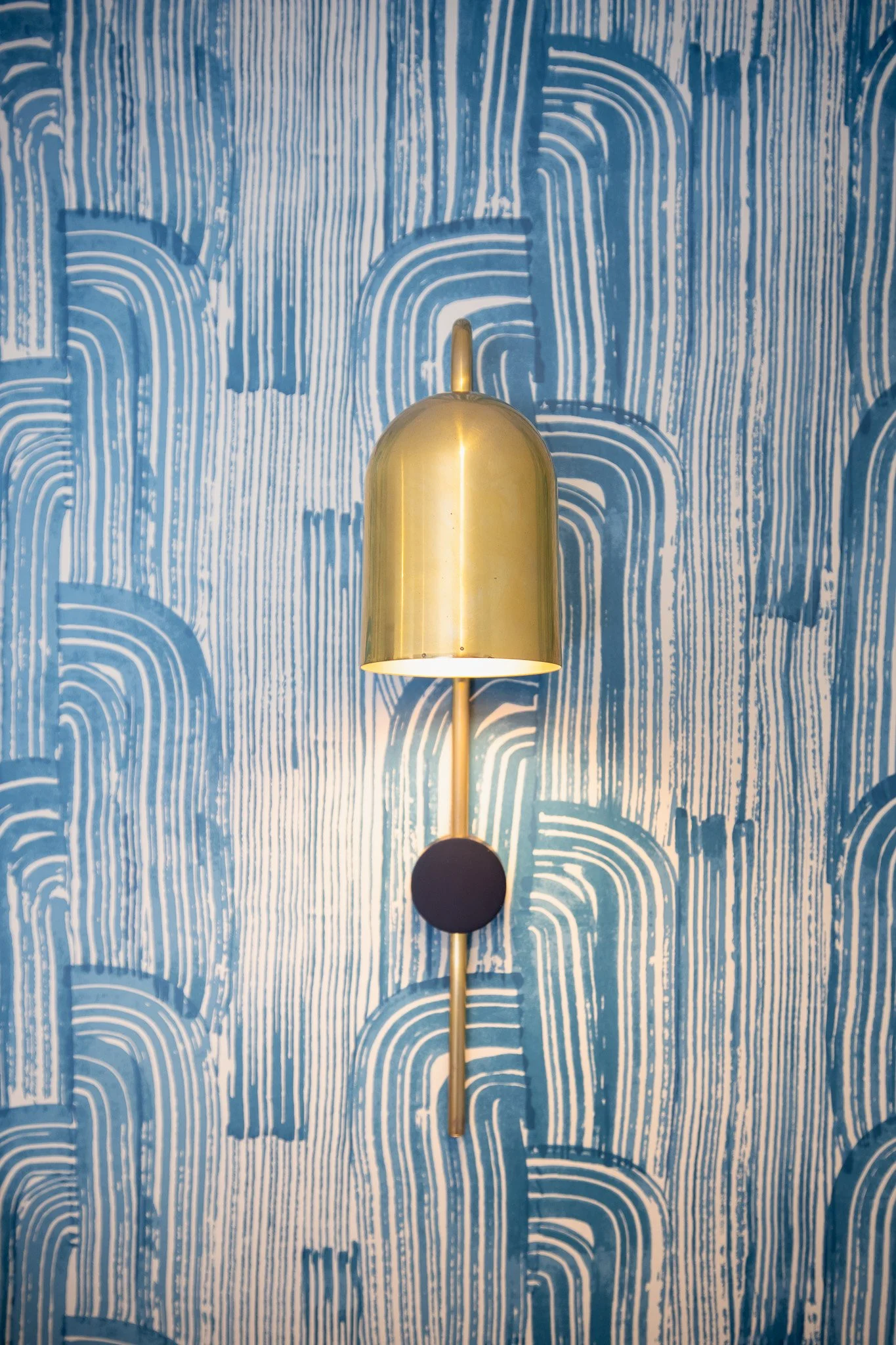 A modern wall-mounted lamp with a gold finish on a textured blue and white patterned wall.