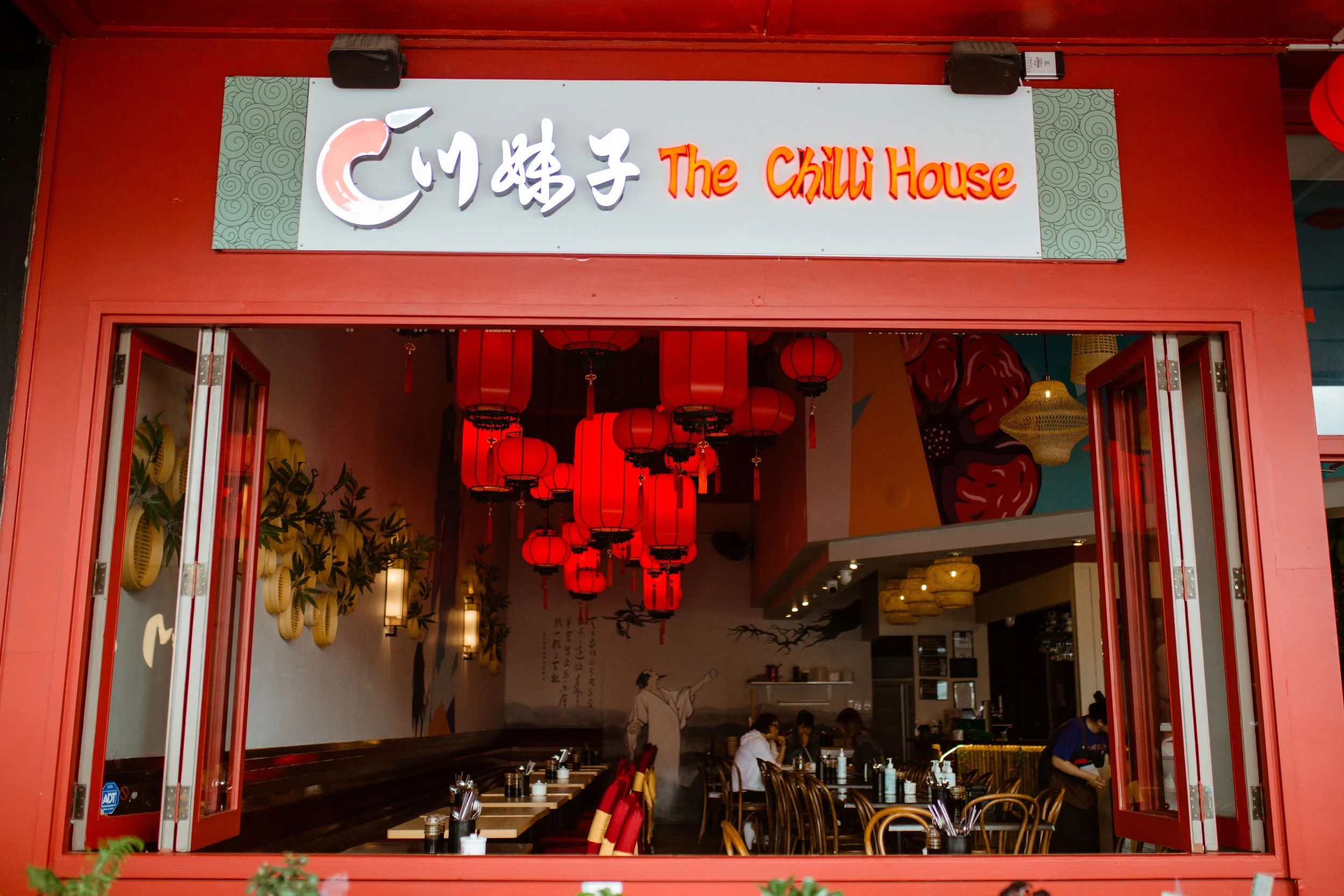 Open restaurant with red lantern decorations and wooden tables inside. The sign above the entrance reads 'City 蜀子 The Chilli House'.