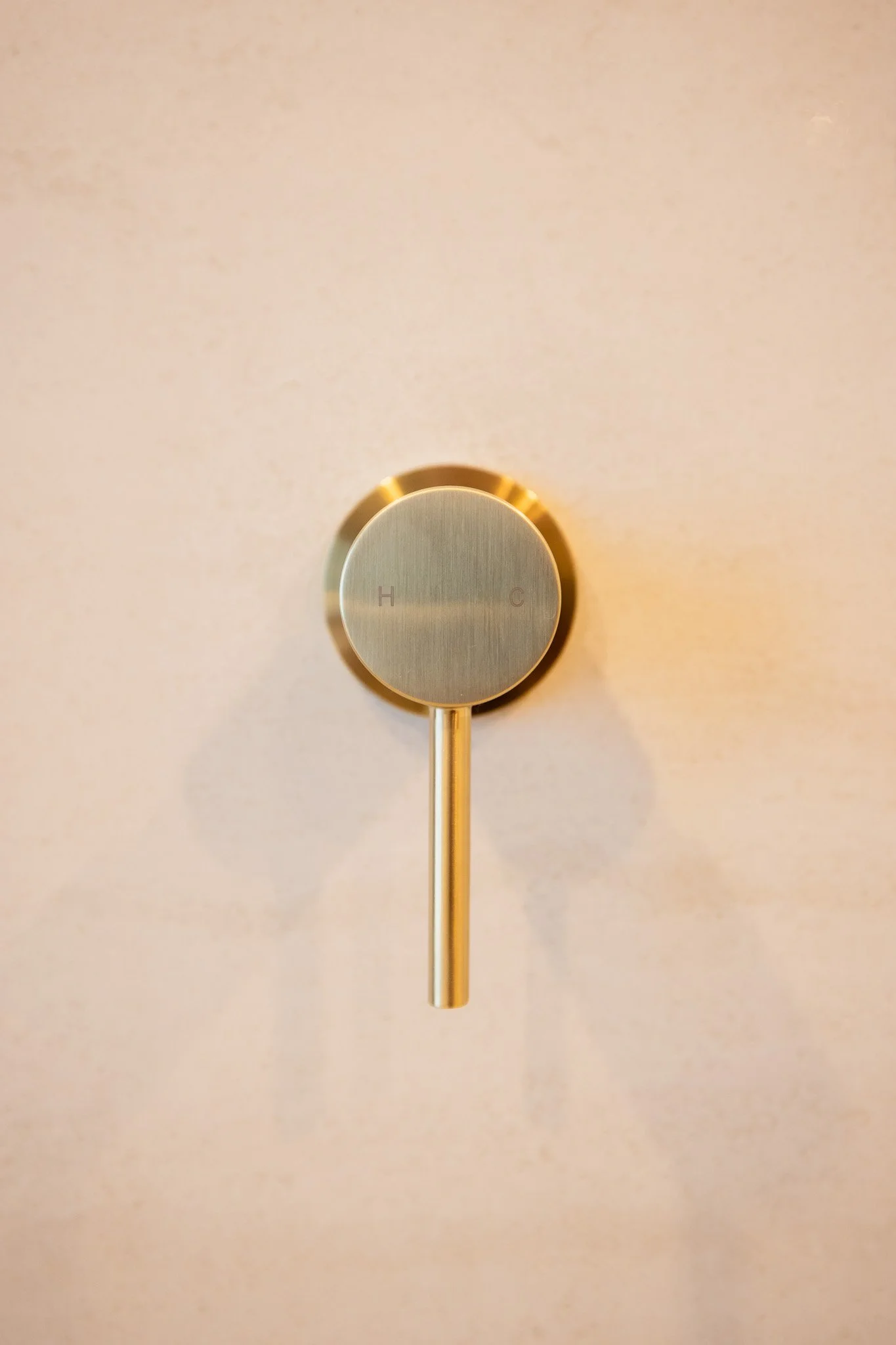 A close-up of a metallic thermostat with a handle and a brushed finish, mounted on a light-colored wall. The dial has markings 'H' for hot and 'C' for cold.