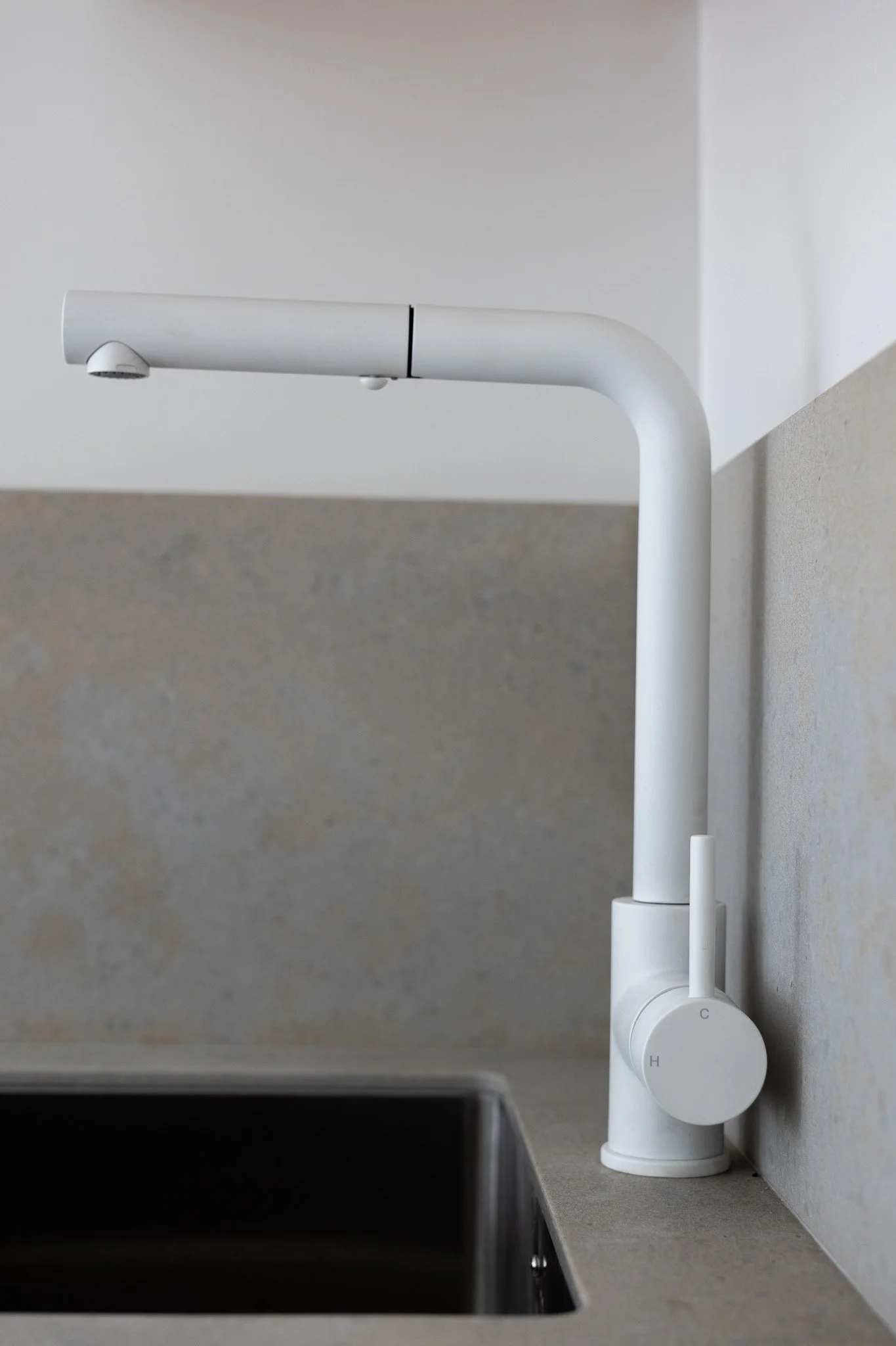 Modern white kitchen faucet mounted on a gray countertop with a sink, against a gray and white wall background.