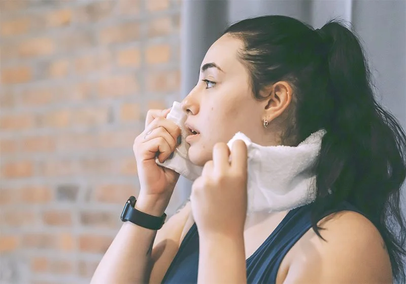 Woman with ponytail, wiping sweat from her face with a towel