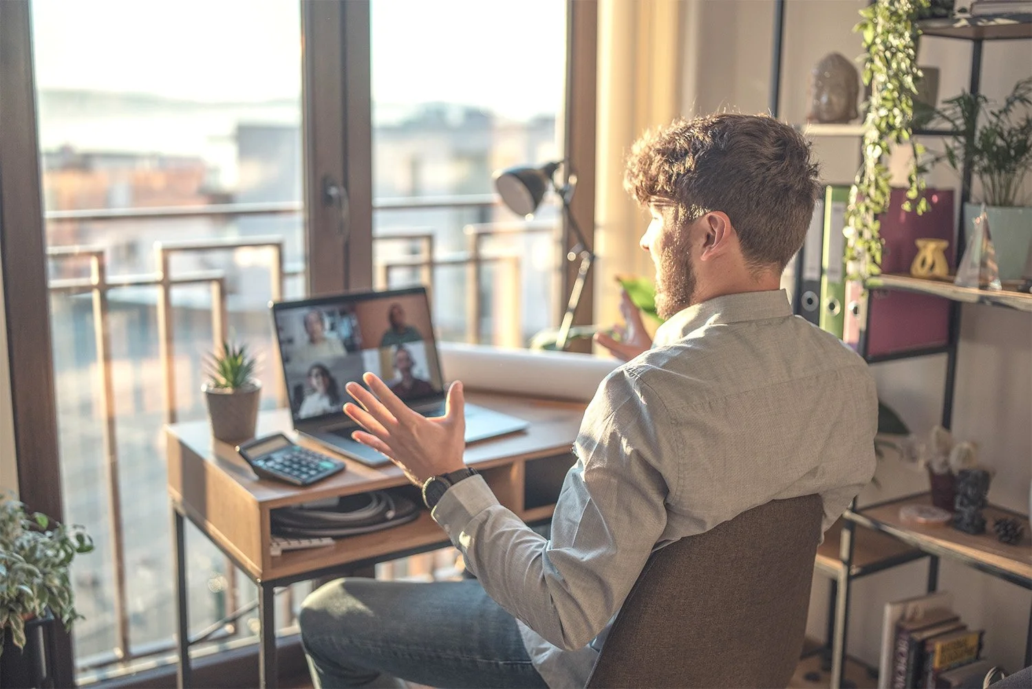 Younger man talking and gesturing to people during a meeting on his laptop screen