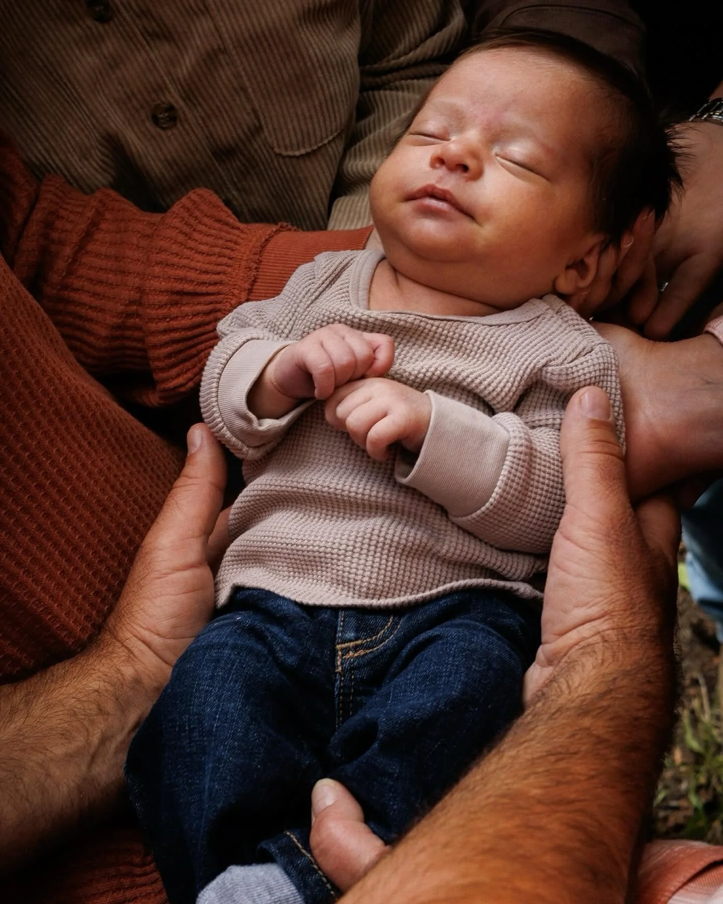 Close-up of a sleeping infant being gently held by multiple hands.