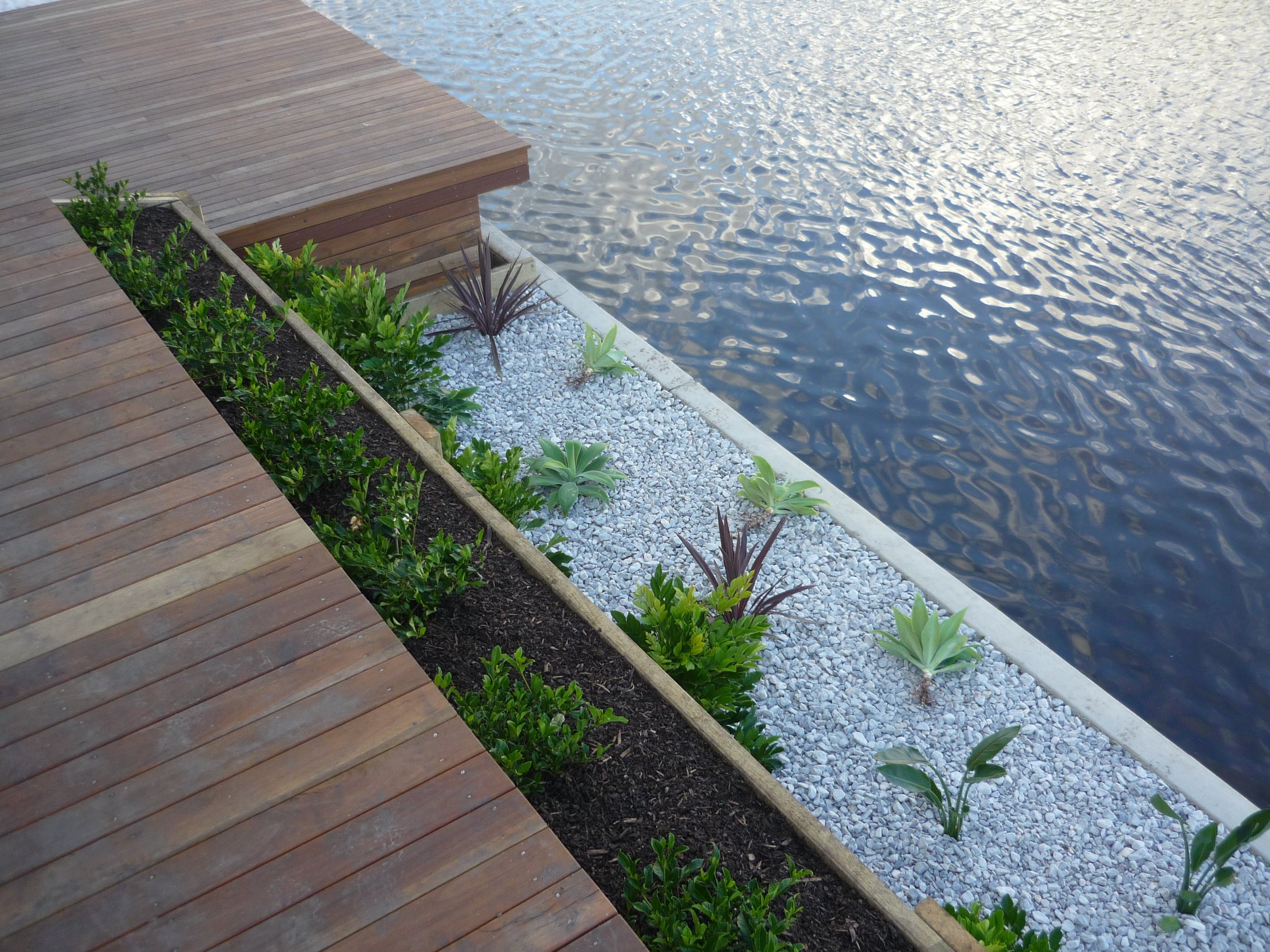Aluminium landscape edging defining a planted garden bed beside a waterfront deck