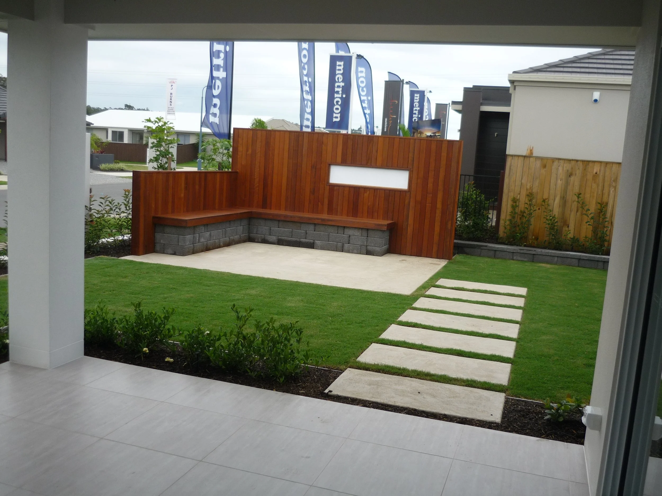 Modern backyard with a lawn, concrete stepping stones, a wooden and stone privacy wall, and a concrete patio.