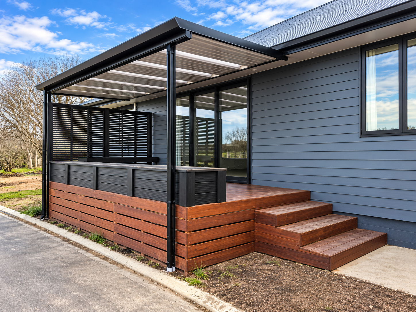 Modern house exterior with a blue siding wall, a wooden porch with steps, a glass sliding door, a black metal and wood railing, and a transparent roof over the porch. Trees and sky in the background.