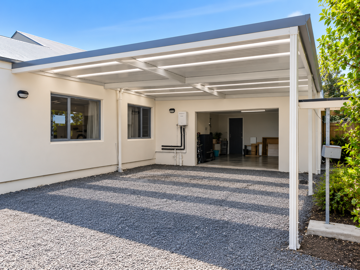 Newly built house with a covered carport, gravel driveway, and open garage with interior shelves and furniture.