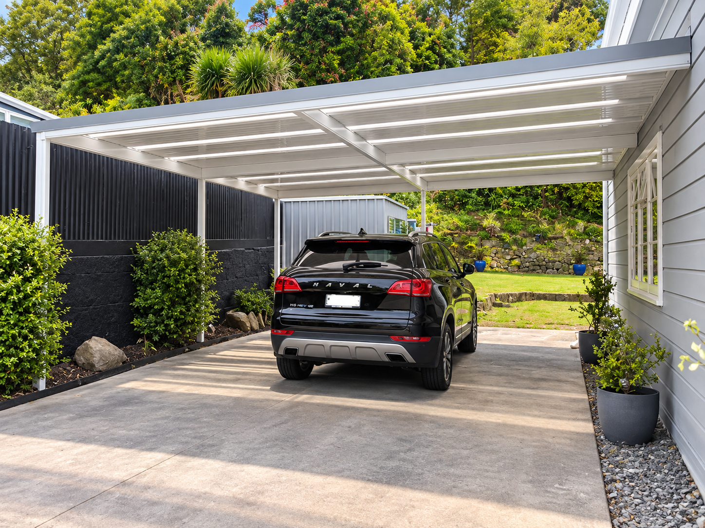 A black Hyundai Santa Fe SUV parked in a modern carport with a white ceiling and black and white walls. There are potted plants along the house wall and landscaped greenery in the background.
