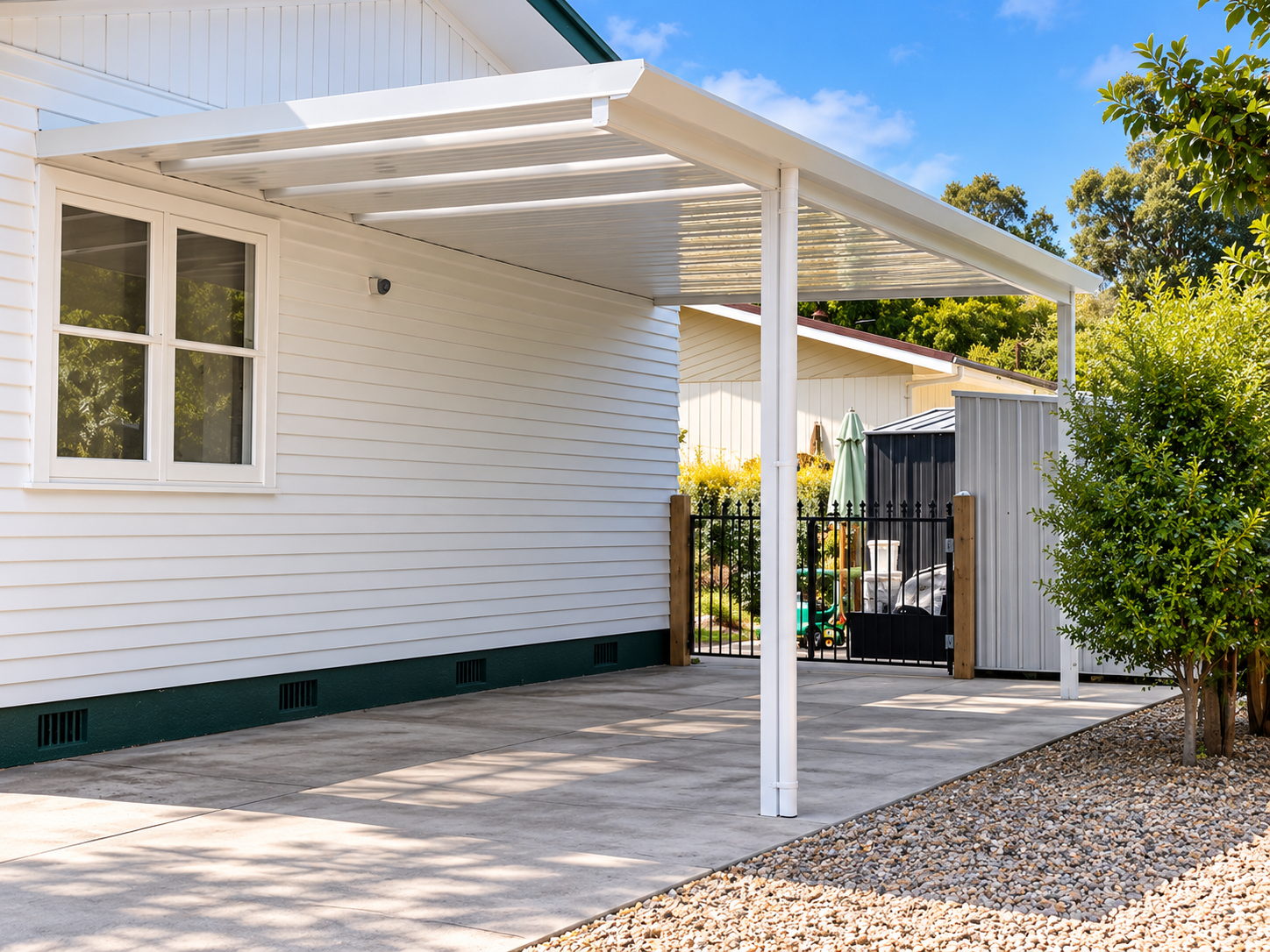 View of a house exterior with a white covered patio and a black gate leading to a backyard with toys and greenery.