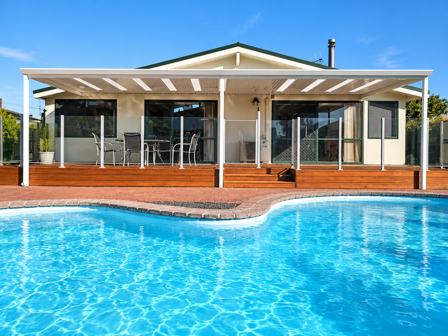 House with screened porch, wooden deck, outdoor furniture, and swimming pool in backyard with clear blue sky.
