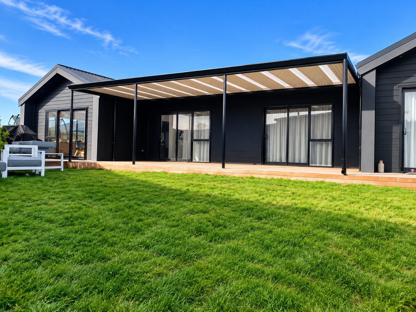 Modern black house with a patio and green lawn under a blue sky.