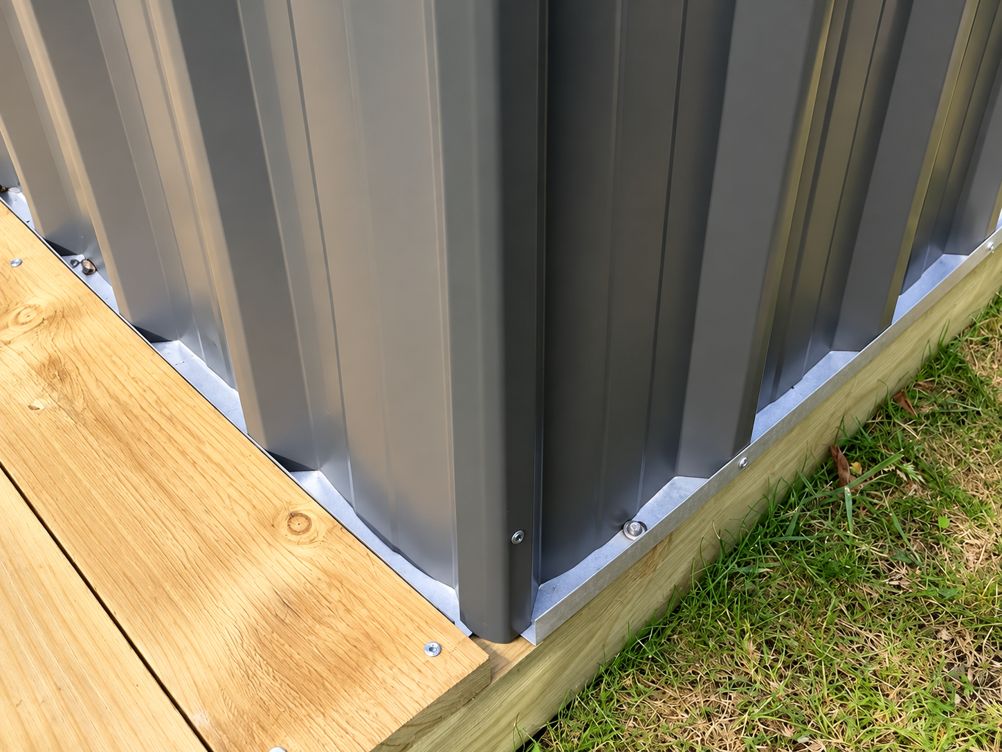 Close-up of a metal structure with vertical panels, mounted on a wooden base, with some screws, next to grass.