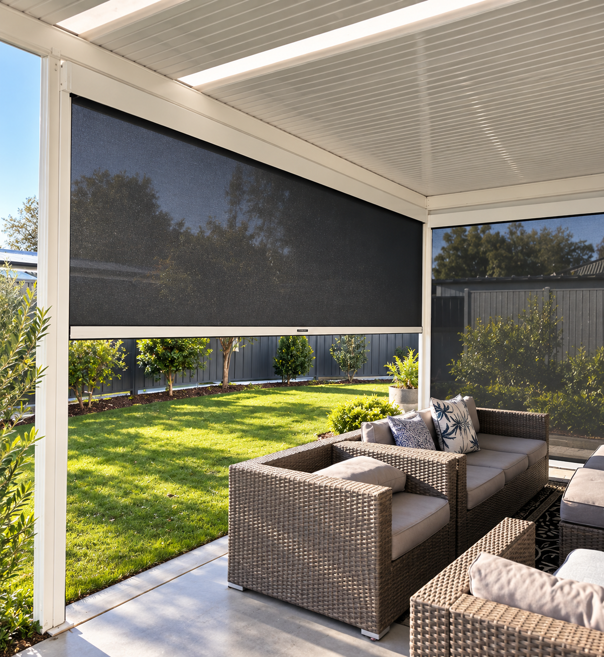 Outdoor patio with wicker furniture and cushions, enclosed by screens, overlooking a garden with trees and grass.