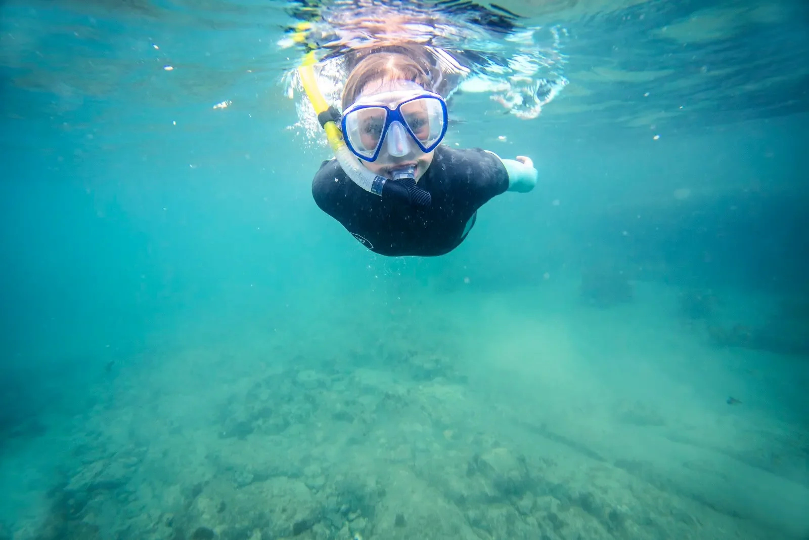 A young girl snorkeling in the clear waters of Goat Island near Auckland, swimming above a soft sandy seabed while wearing a snorkeling mask.