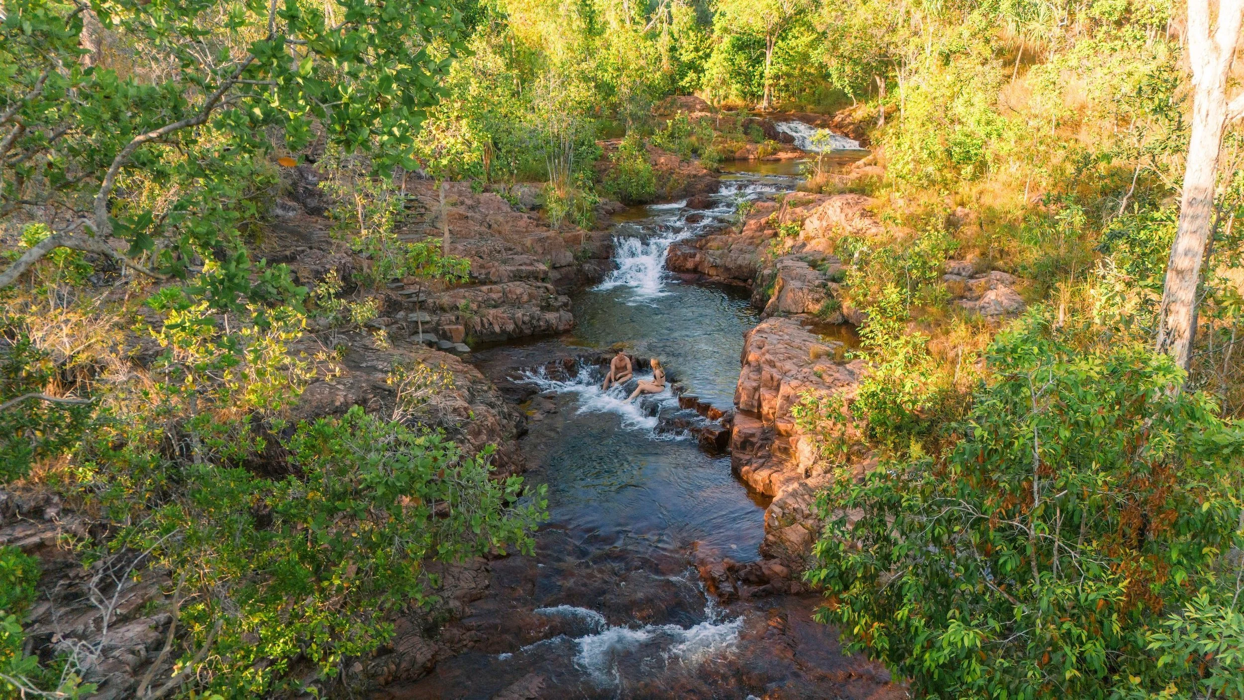 Two people relax in the clear waters of Buley Rockhole, Litchfield National Park, Northern Territory, Australia, surrounded by lush greenery and natural rock pools.