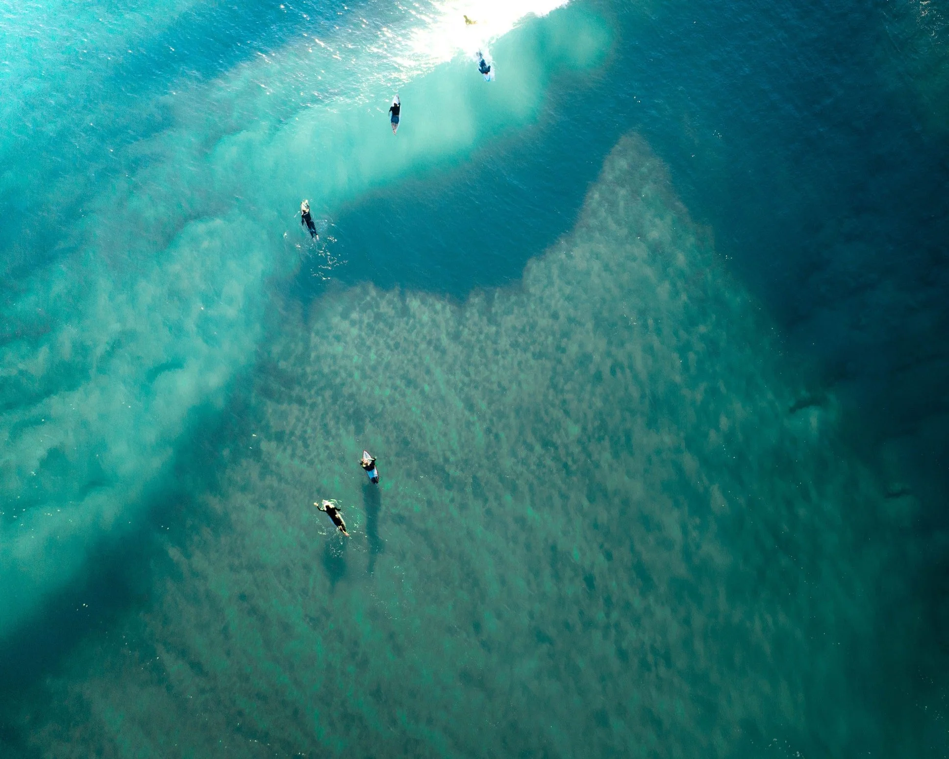 Aerial view of a lone surfer waiting for waves at sunrise, bathed in golden light off the coast of Sydney, Australia.