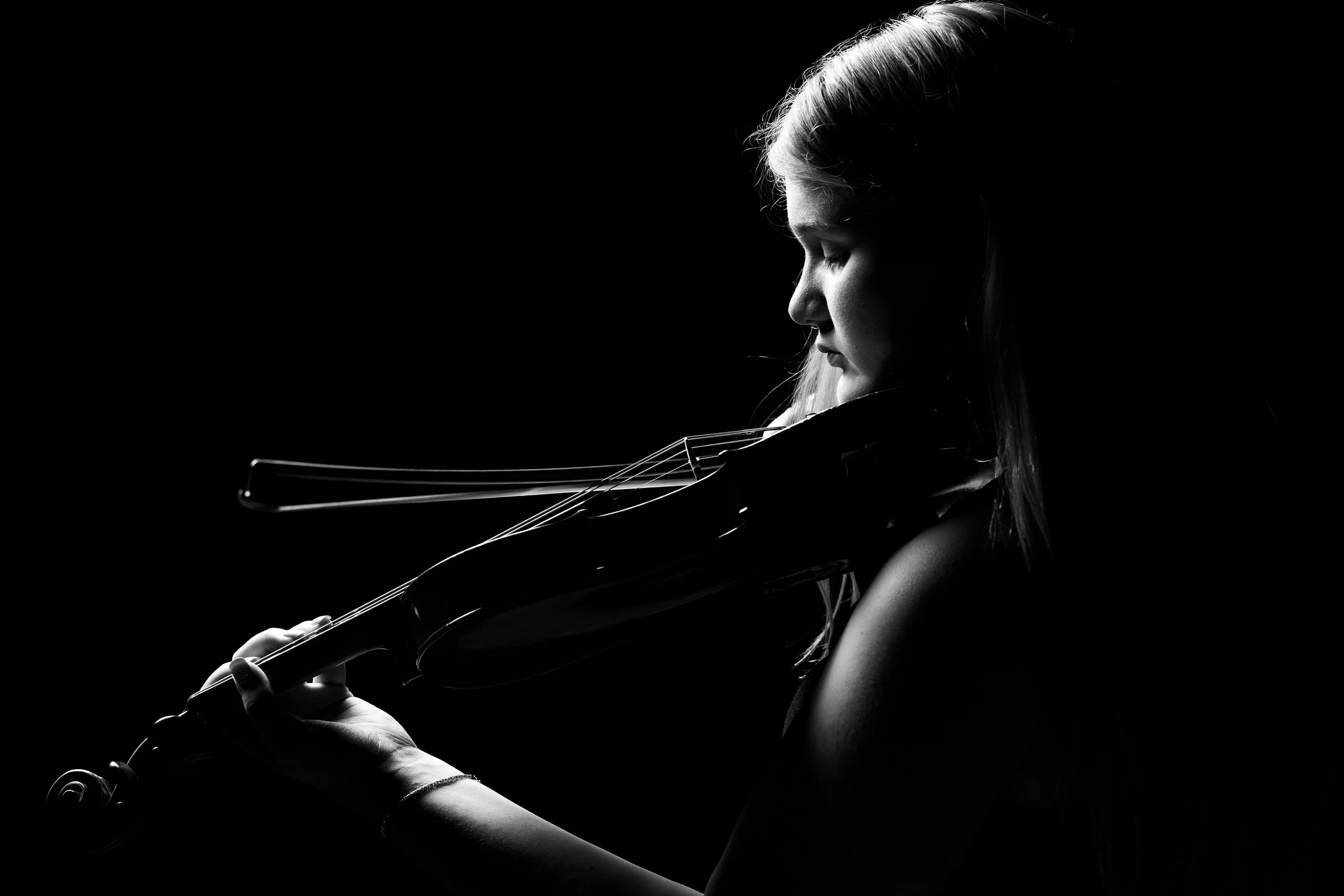 Silhouette of a woman playing a violin against a black background, with side lighting highlighting her face and the violin.