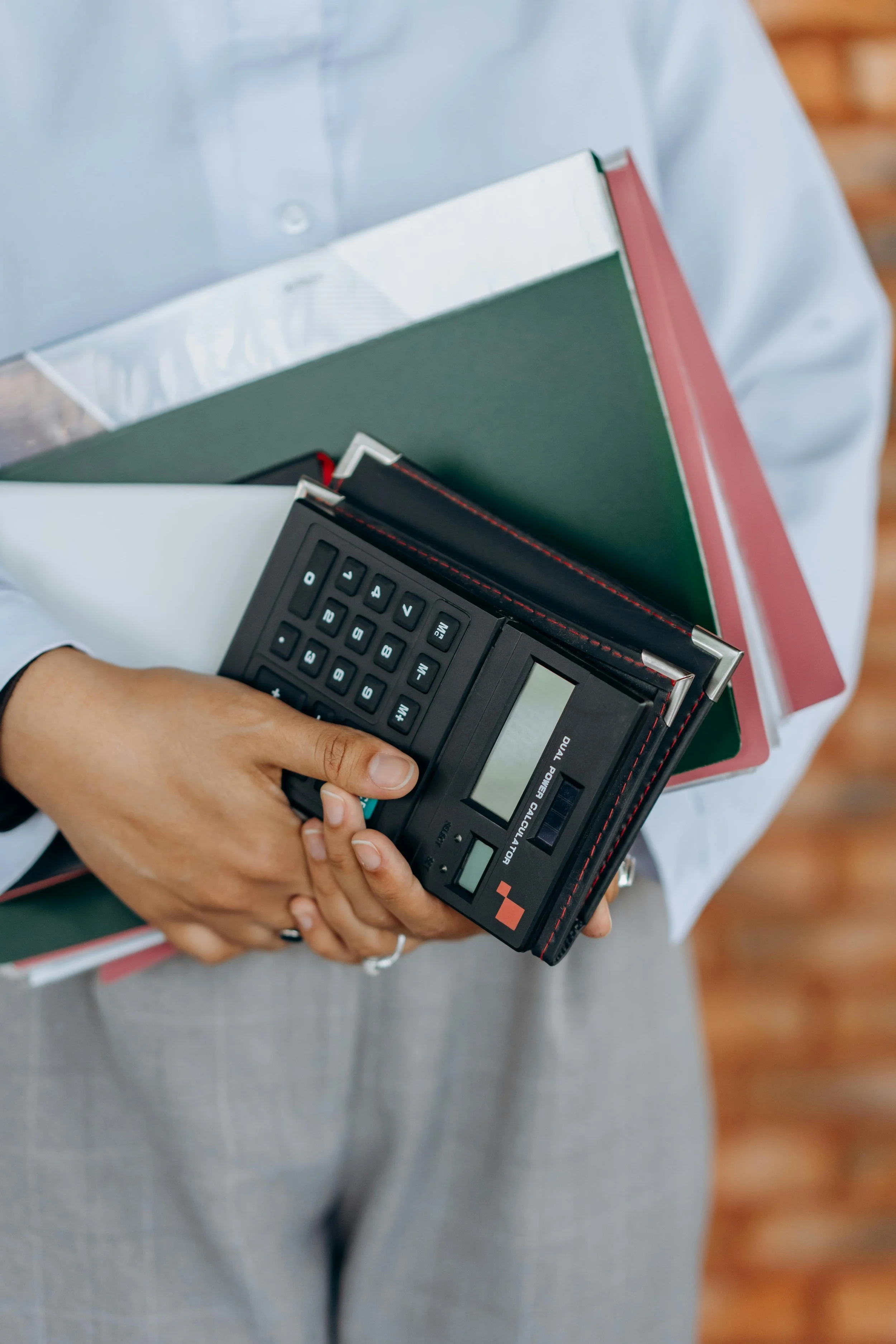 A woman's hand holding several folders and documents and a calculator
