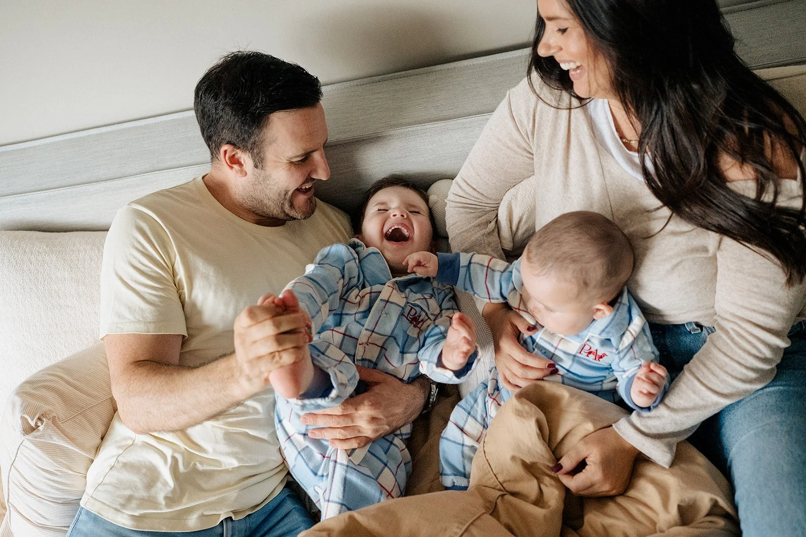 Mother, father and kids having a laugh and a play on their bed and the kids are in matching pjs during an in-home family photography session in Melbourne