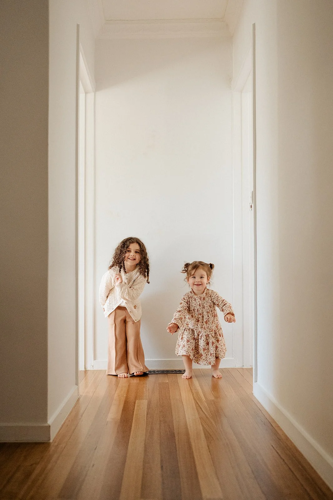 Two little sisters running up the hallway during an in-home family photography session in Melbourne