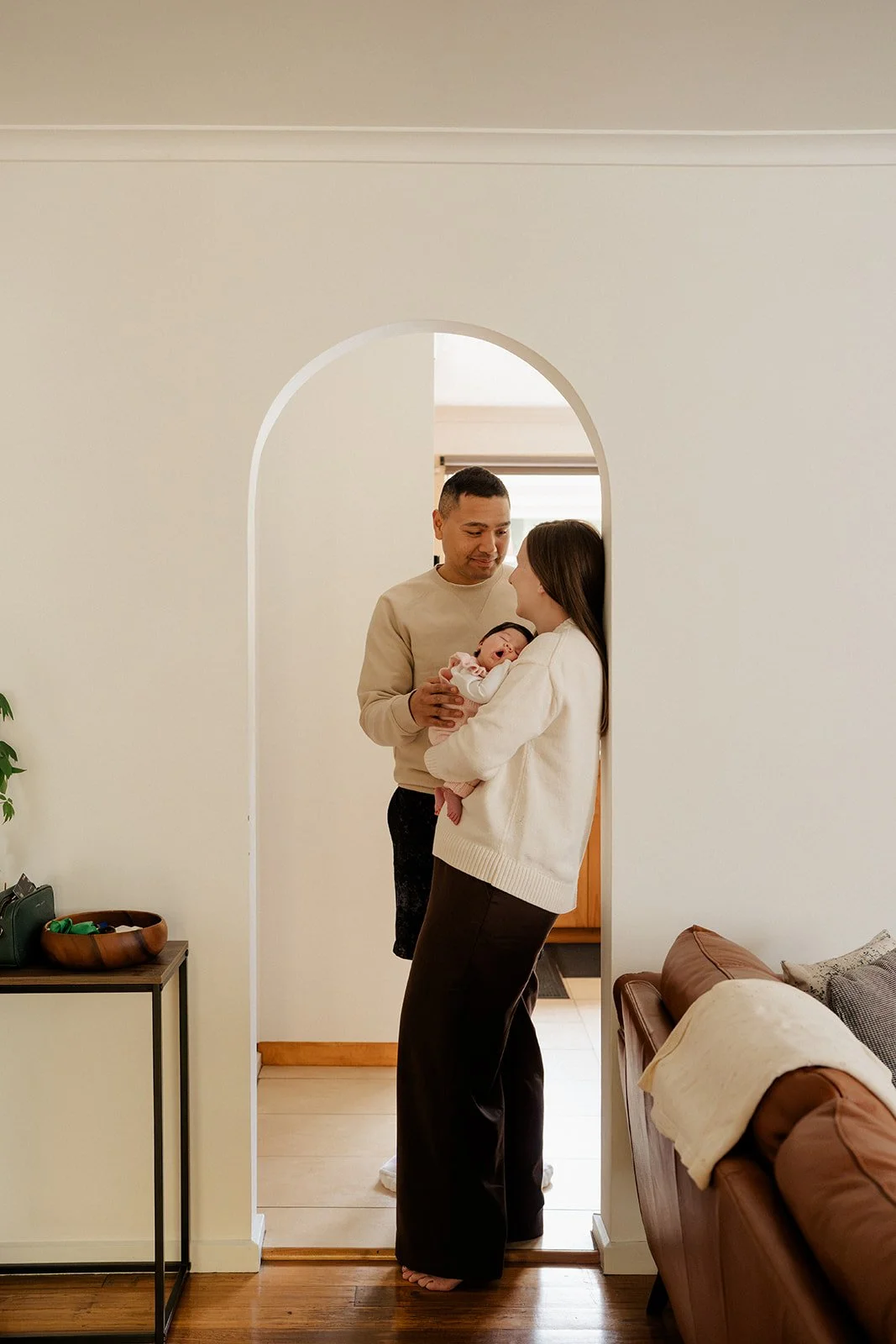 Parents holding their newborn baby in a cozy home doorway during an in-home newborn photography session in Melbourne.
