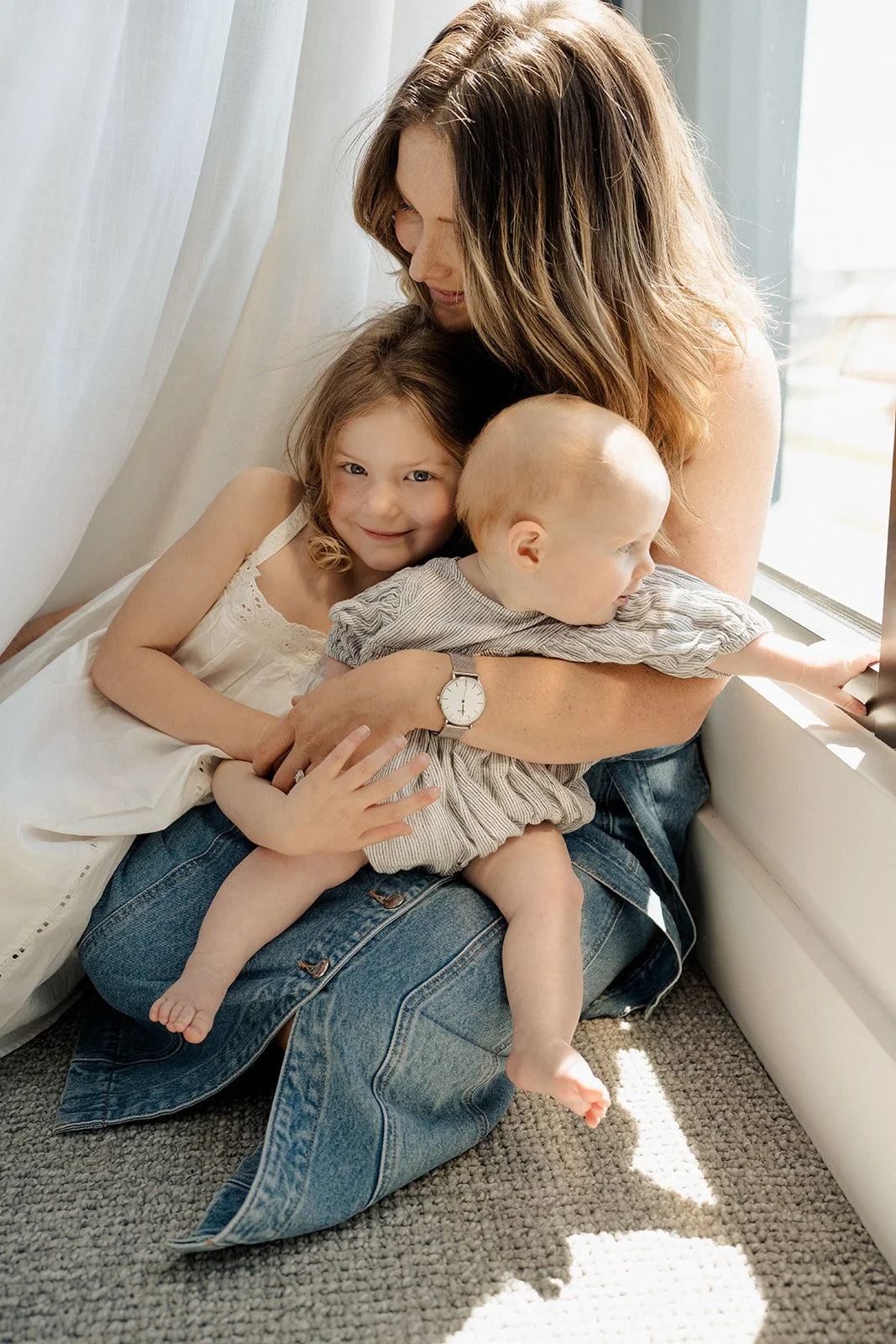 Mother embracing her two young children by a sunlit window during an in-home motherhood photography session in Melbourne.