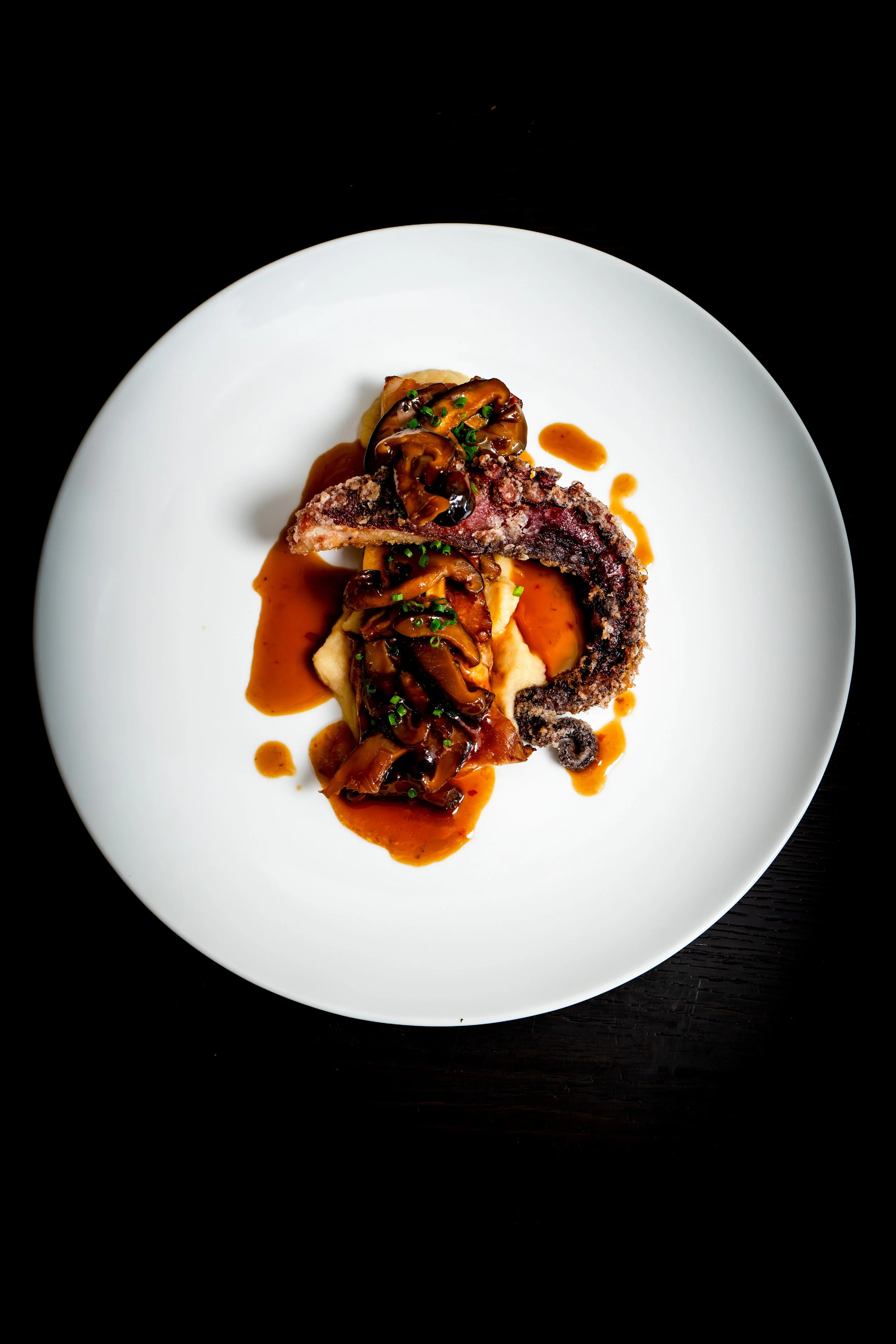 Gebratenes Meeresfrüchtegericht mit Tintenfisch, Pilzsauce und Kartoffelpüree auf einem weißen Teller.