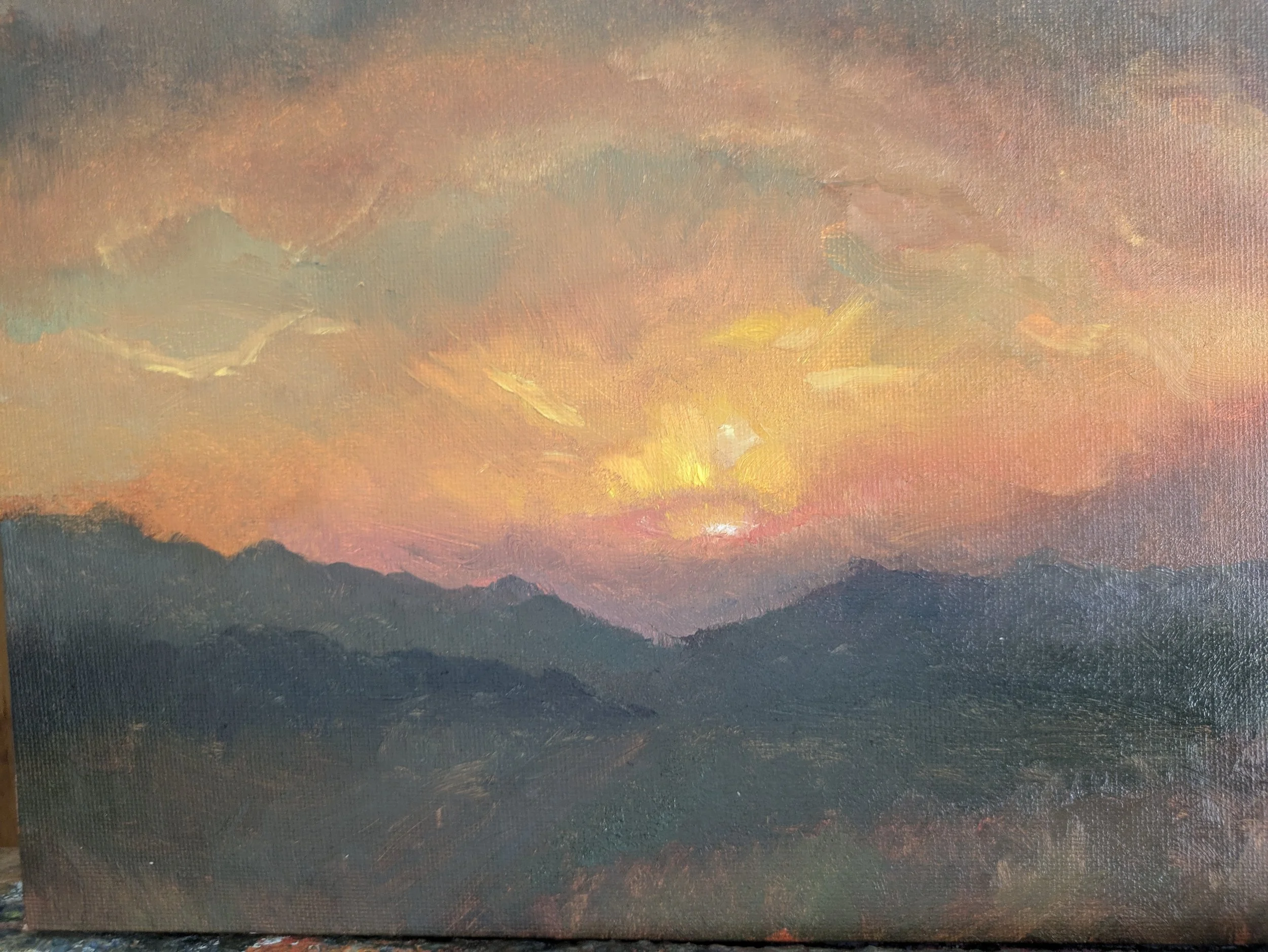 A sunset or sunrise over mountains, with warm colors in the sky and dark silhouettes of the mountain range.
