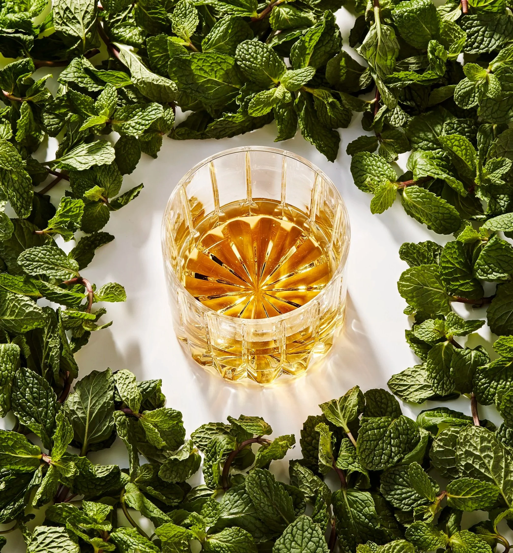 Neat whiskey glass with a surface of fresh mint around it - shot for whisky advocate magazine, photographed by Jeff Harris - food styling, commercial food stylist NYC