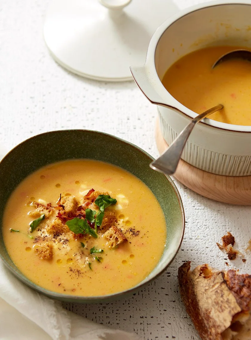 A bowl and pot of roasted pumpkin soup with bacon and bread crumbs on top with a swirl of creme, photographed by Dane Tashima - food styling, commercial food stylist NYC