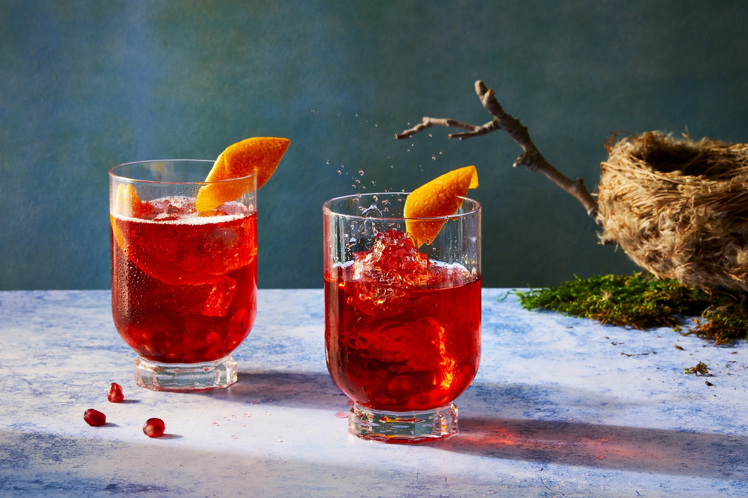 Cocktail concept shoot showing two bright red negroni cocktails with an ice cube dropped into one - food styling, commercial food stylist NYC photographed by Rachel Vanni